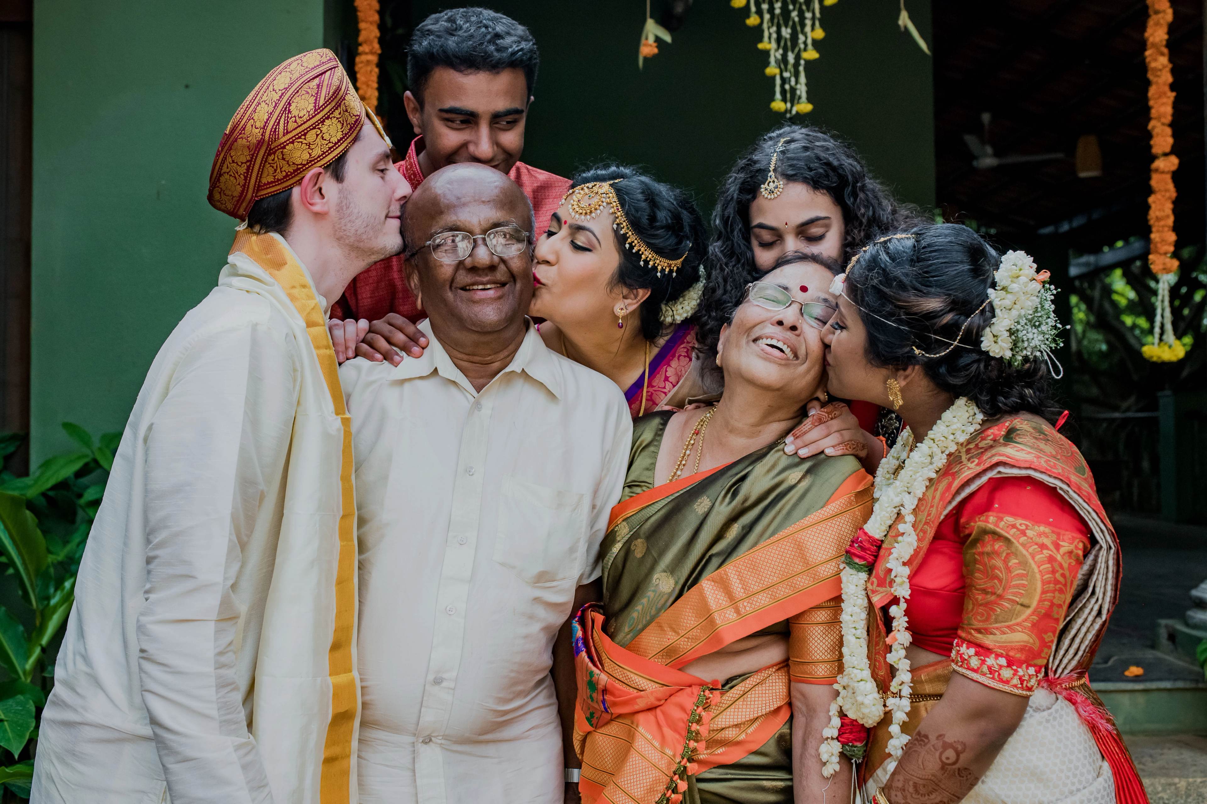Extended family celebrating in traditional Indian attire against green backdrop with marigold garlands