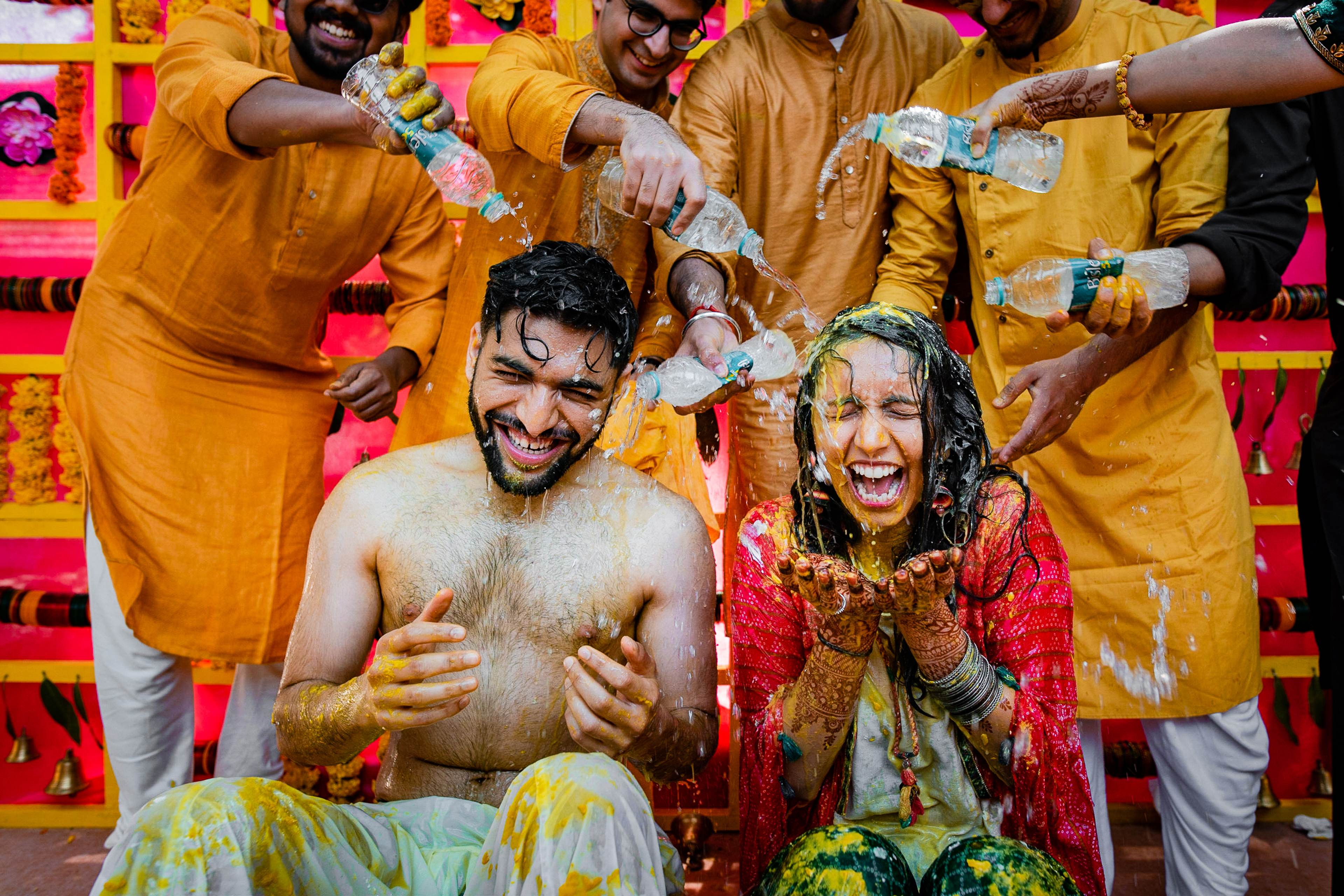 Avani and Srikant laughing while friends in yellow throw colored powder during Holi celebration in Goa