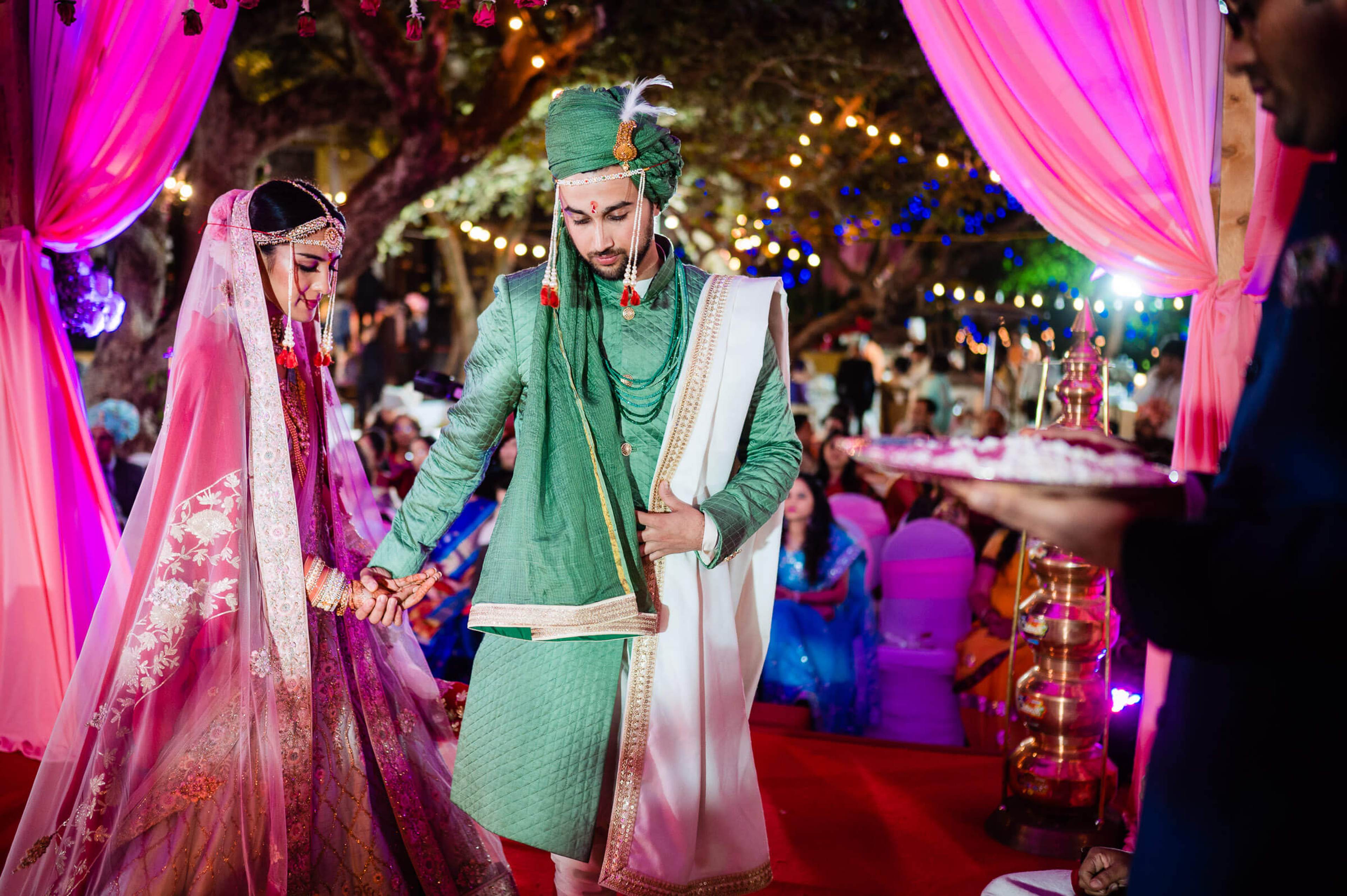 Shreya and Yash in traditional attire walking under neon-lit pink drapes at their Mahabaleshwar wedding celebration