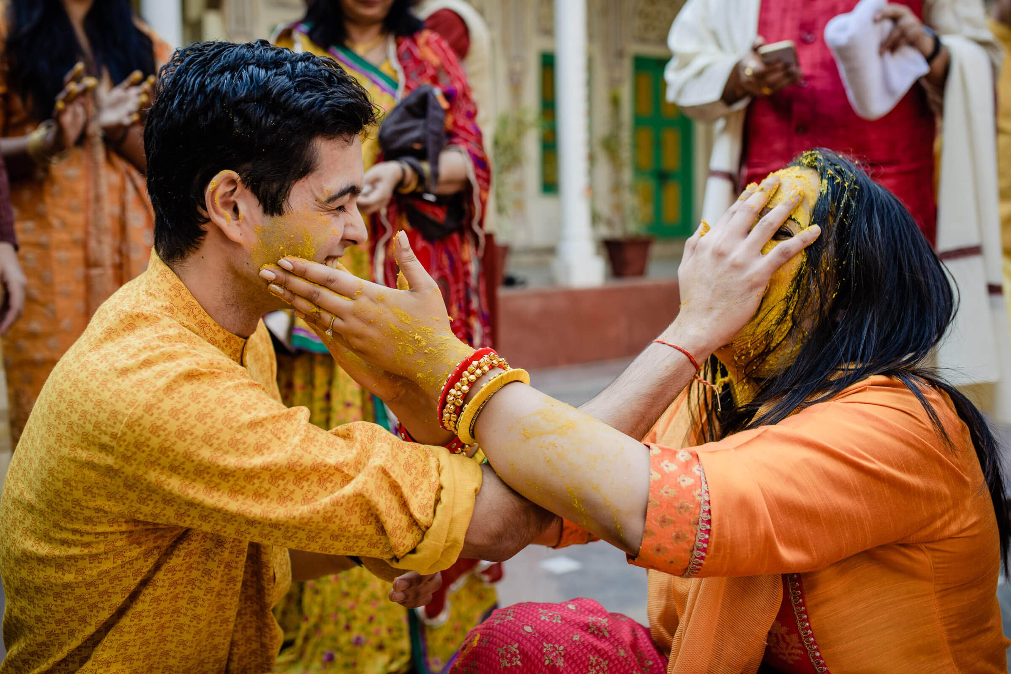 Maitrayee and Eric apply turmeric paste to each other's face during Haldi ceremony in Rajasthan, surrounded by family