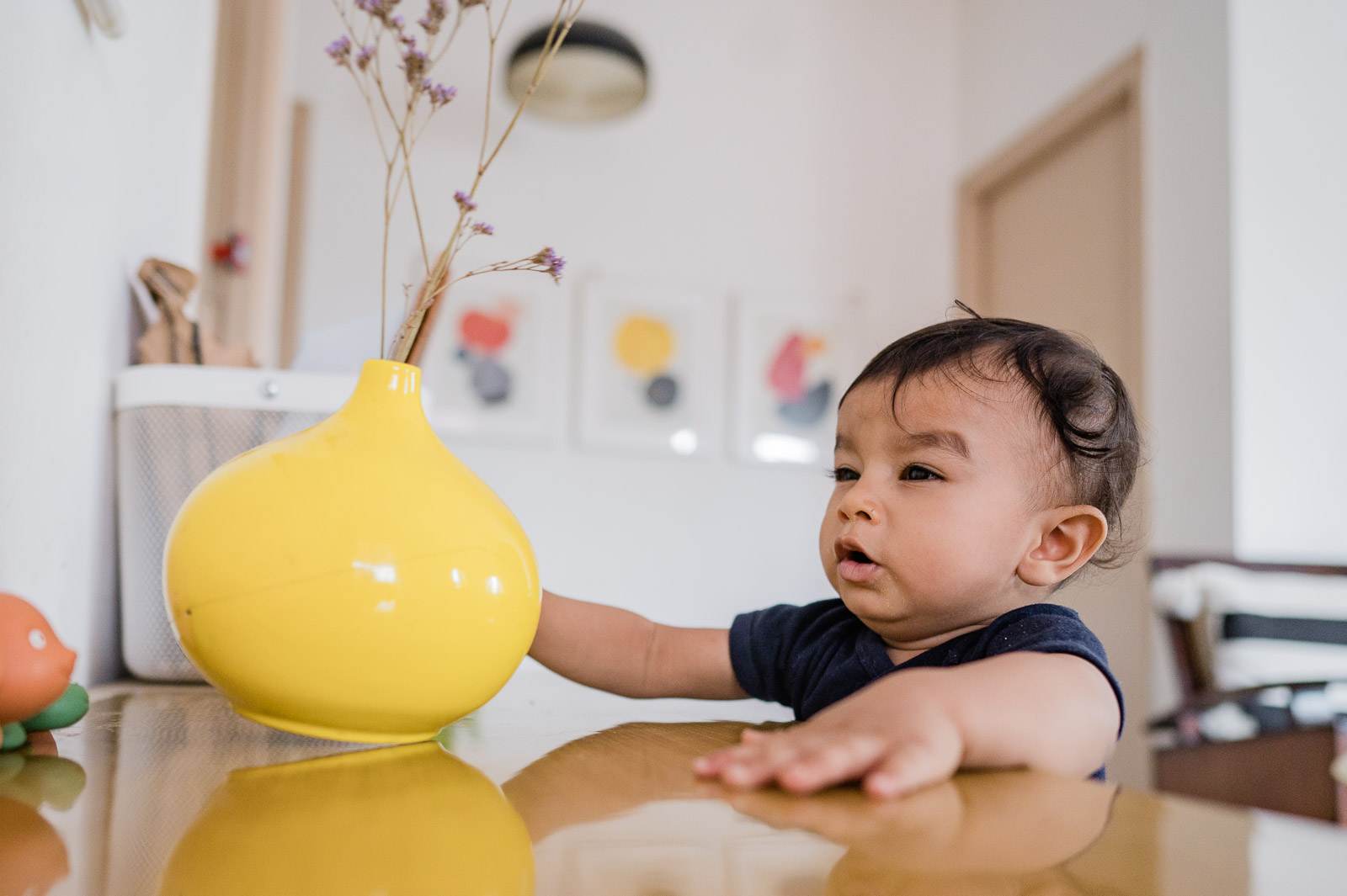Toddler reaching toward a yellow vase with dried flowers on a modern table by Rimi Sen