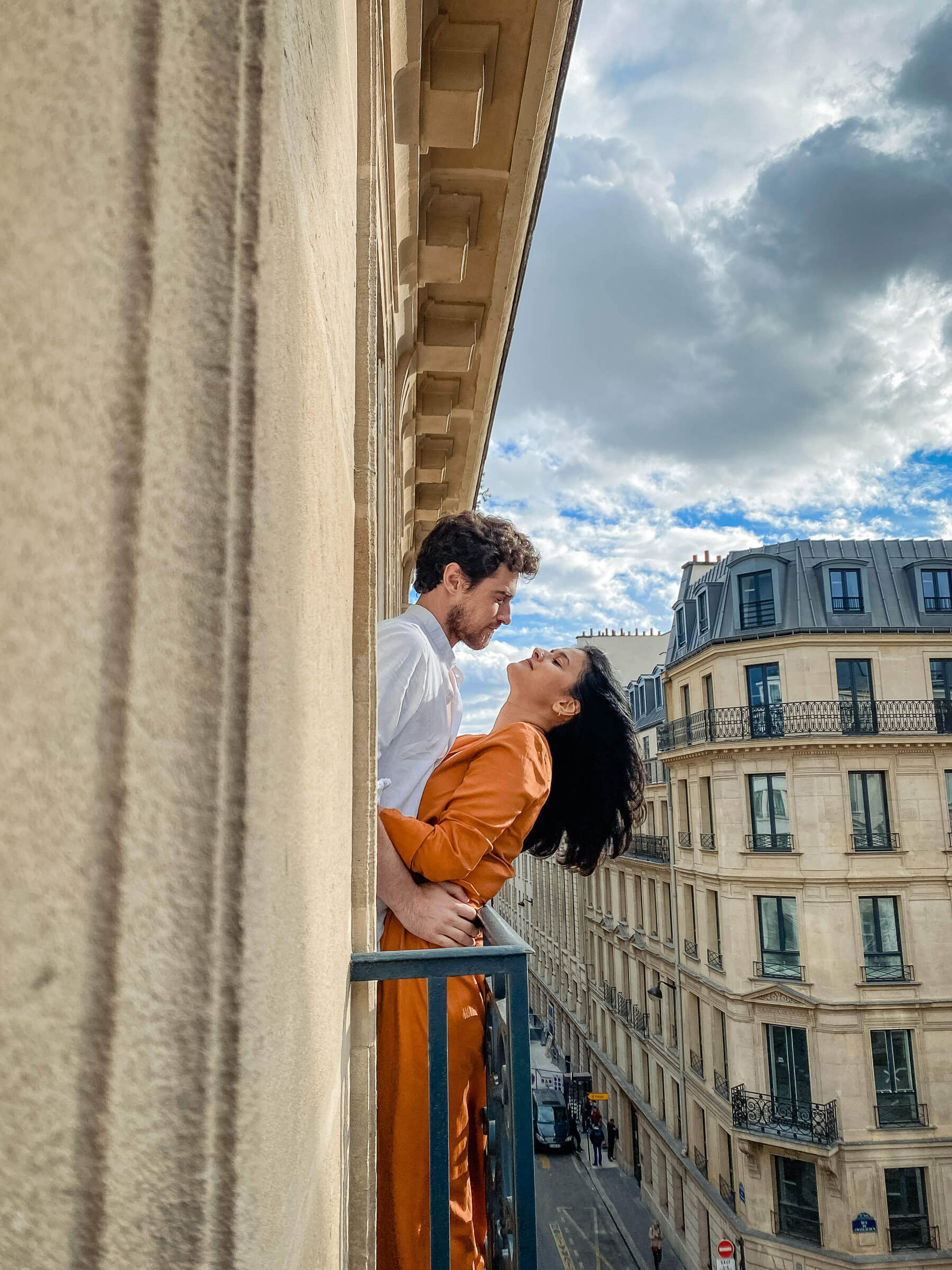 Couple embracing on Parisian balcony overlooking historic architecture and cloudy sky