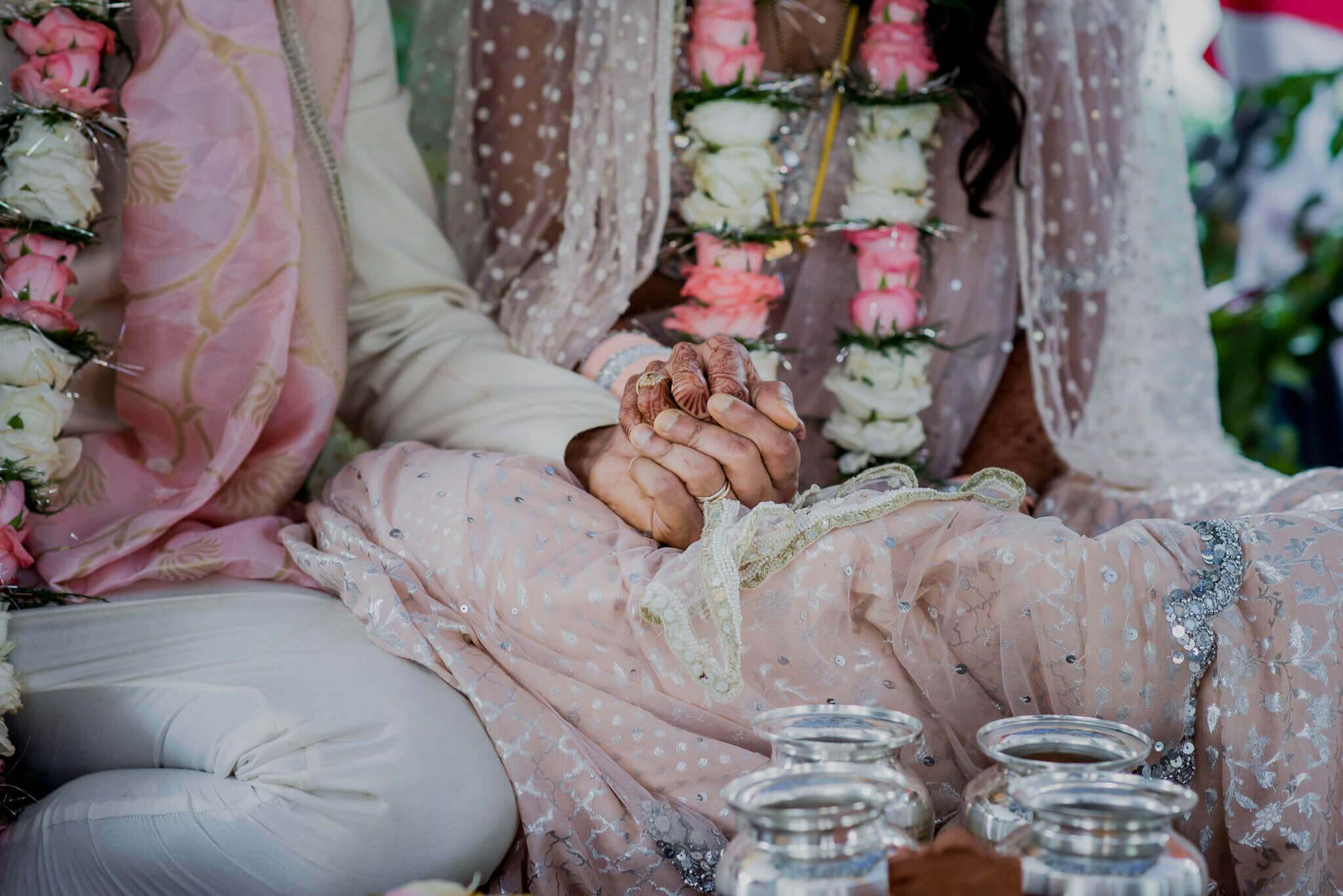 Anu and Raghu hold hands in embellished traditional attire with floral garlands during their Nepal wedding ceremony