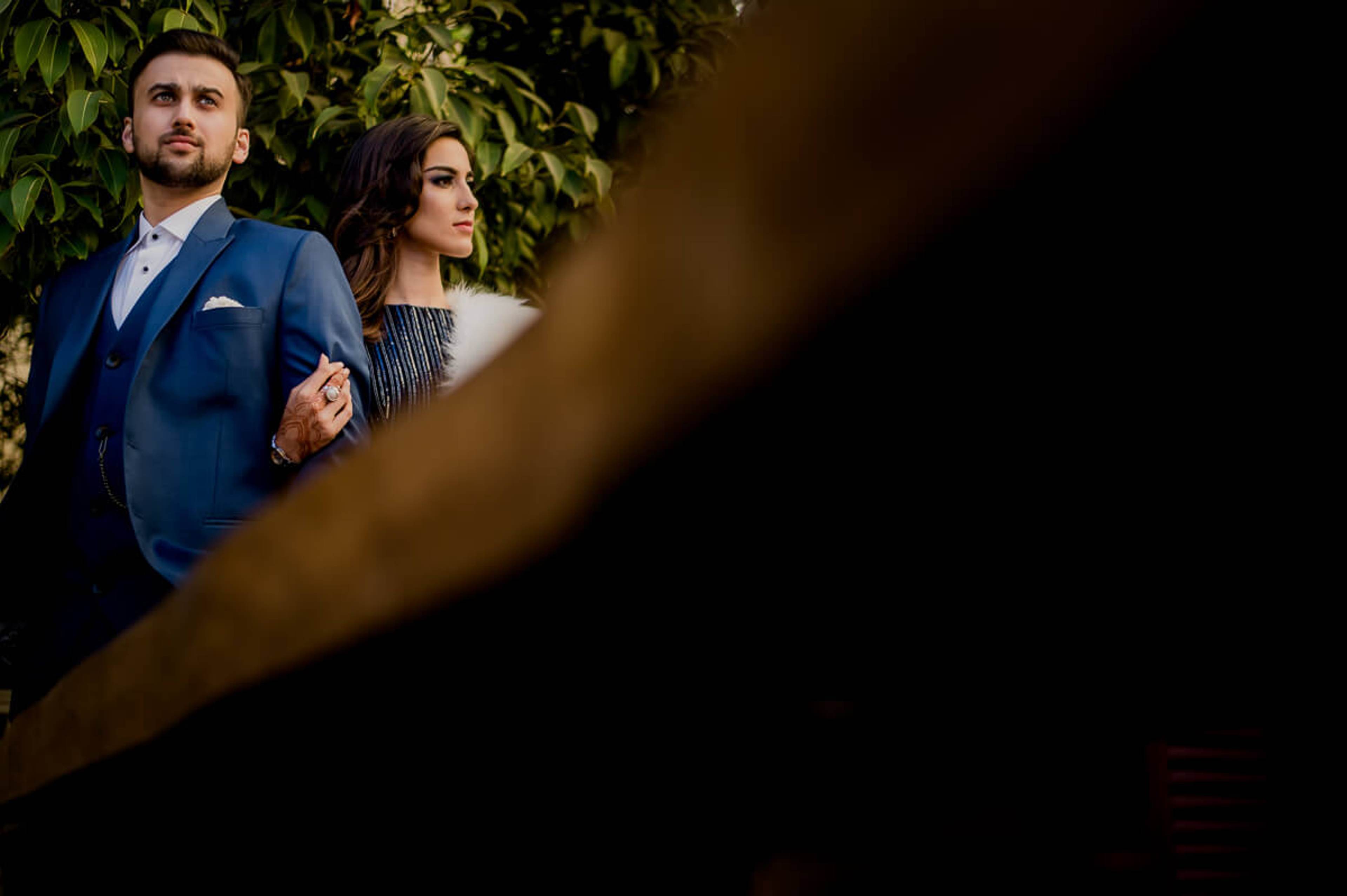Shreya and Yash stand together among lush greenery, framed by foliage in warm evening light