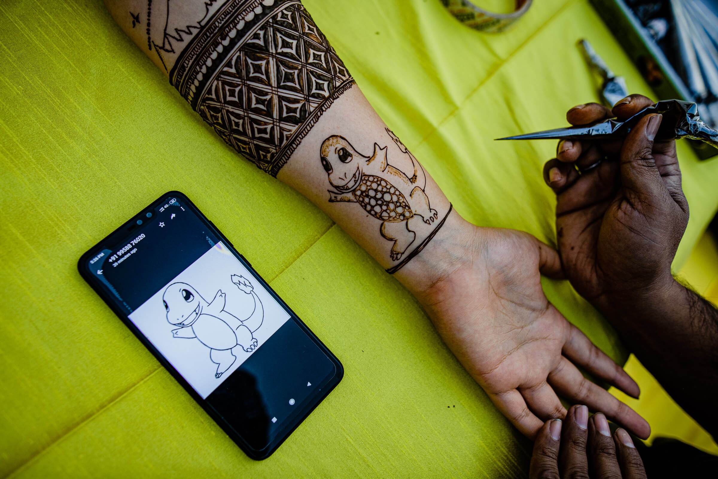 Hand with henna tattoo and phone displaying design sketch on bright yellow fabric in Rajasthan