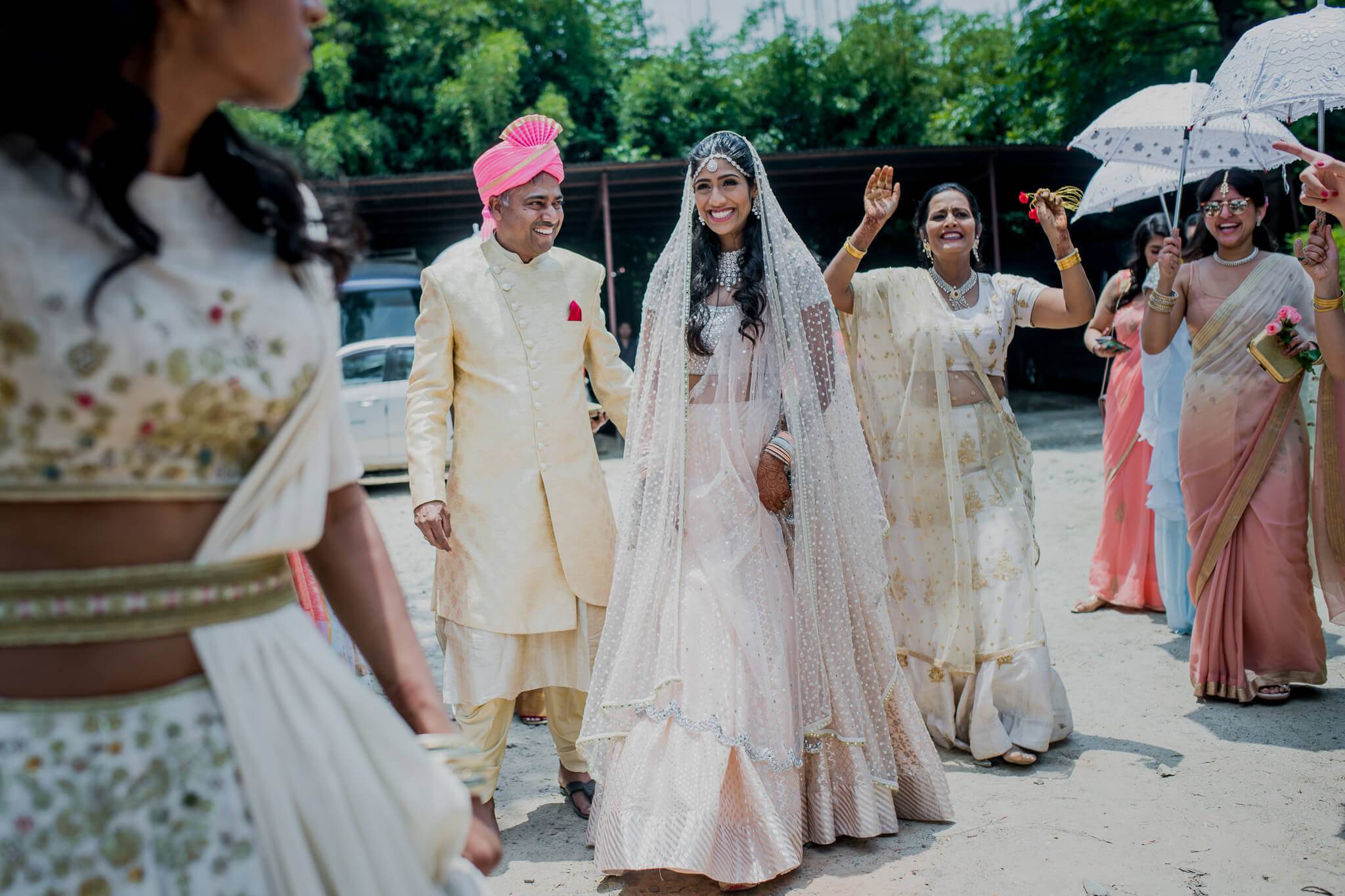 Anu and Raghu walk together in traditional attire surrounded by family with umbrellas at their Nepal wedding celebration