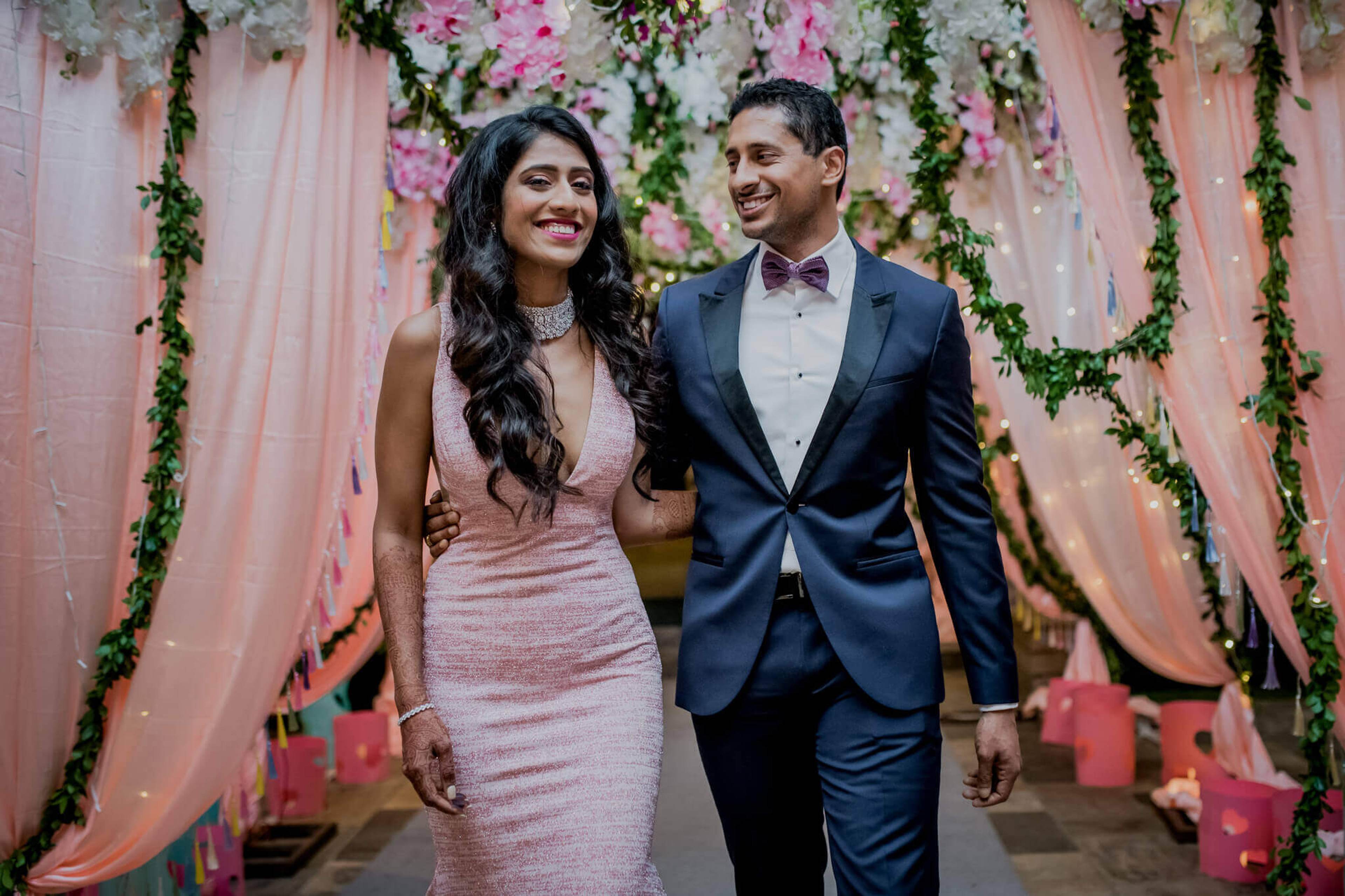 Anu and Raghu walk beneath pink draped fabric and floral garland at their Nepal wedding venue