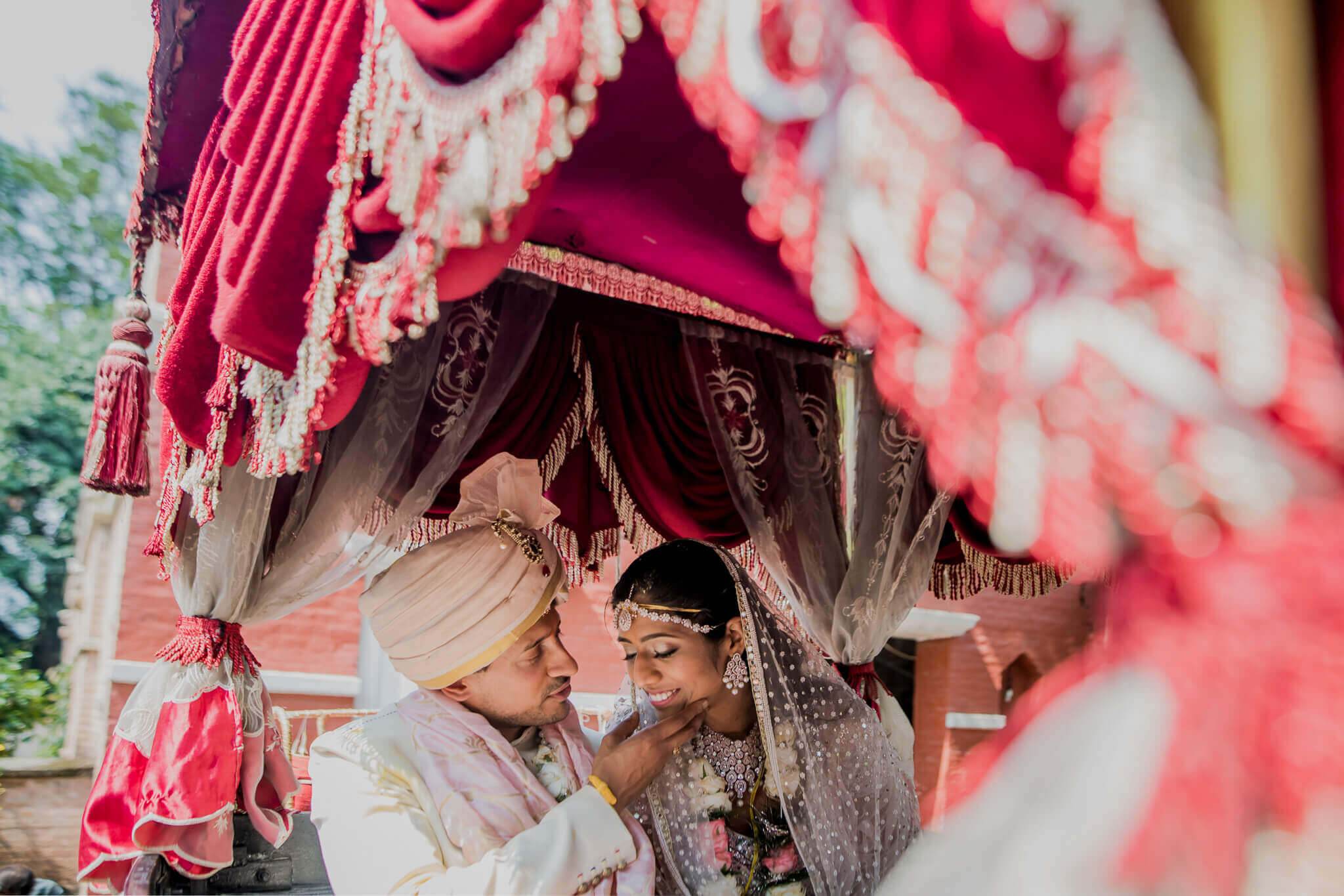 Anu and Raghu sheltered under vibrant pink and red draped fabric during wedding ceremony in Nepal