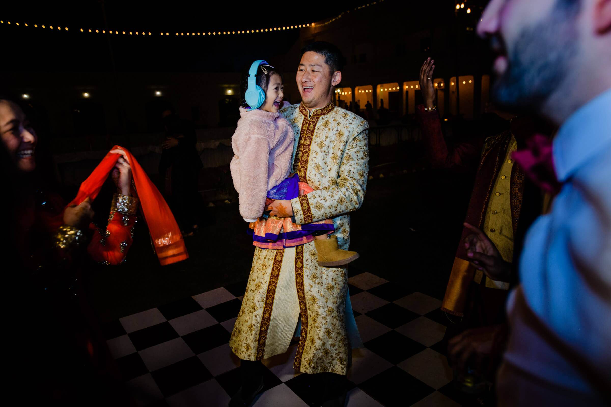Maitrayee and Eric dance at night in traditional Rajasthani attire under string lights, checkered floor