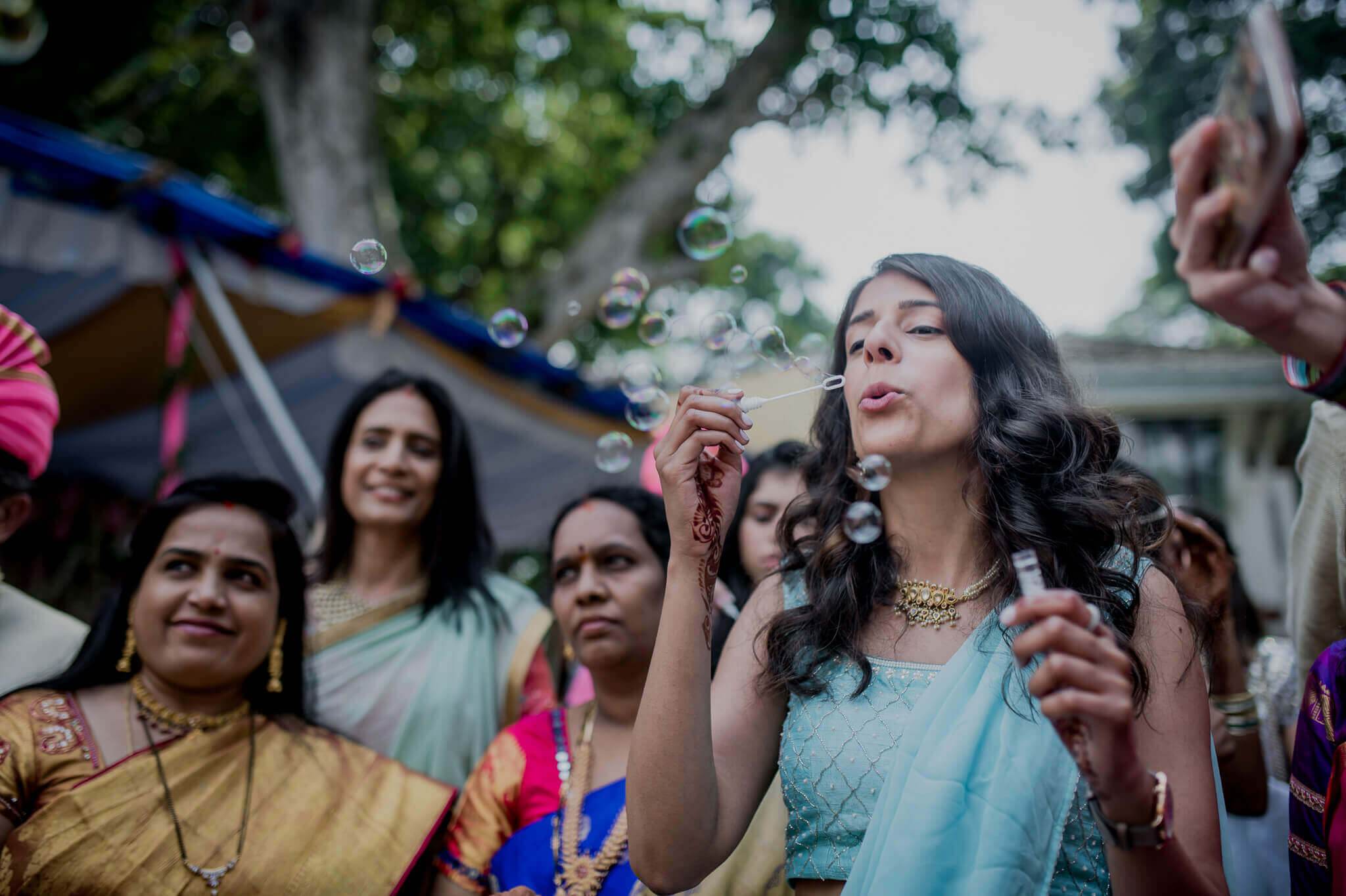 Anu blowing bubbles among family at outdoor celebration in Nepal, wearing light blue dress