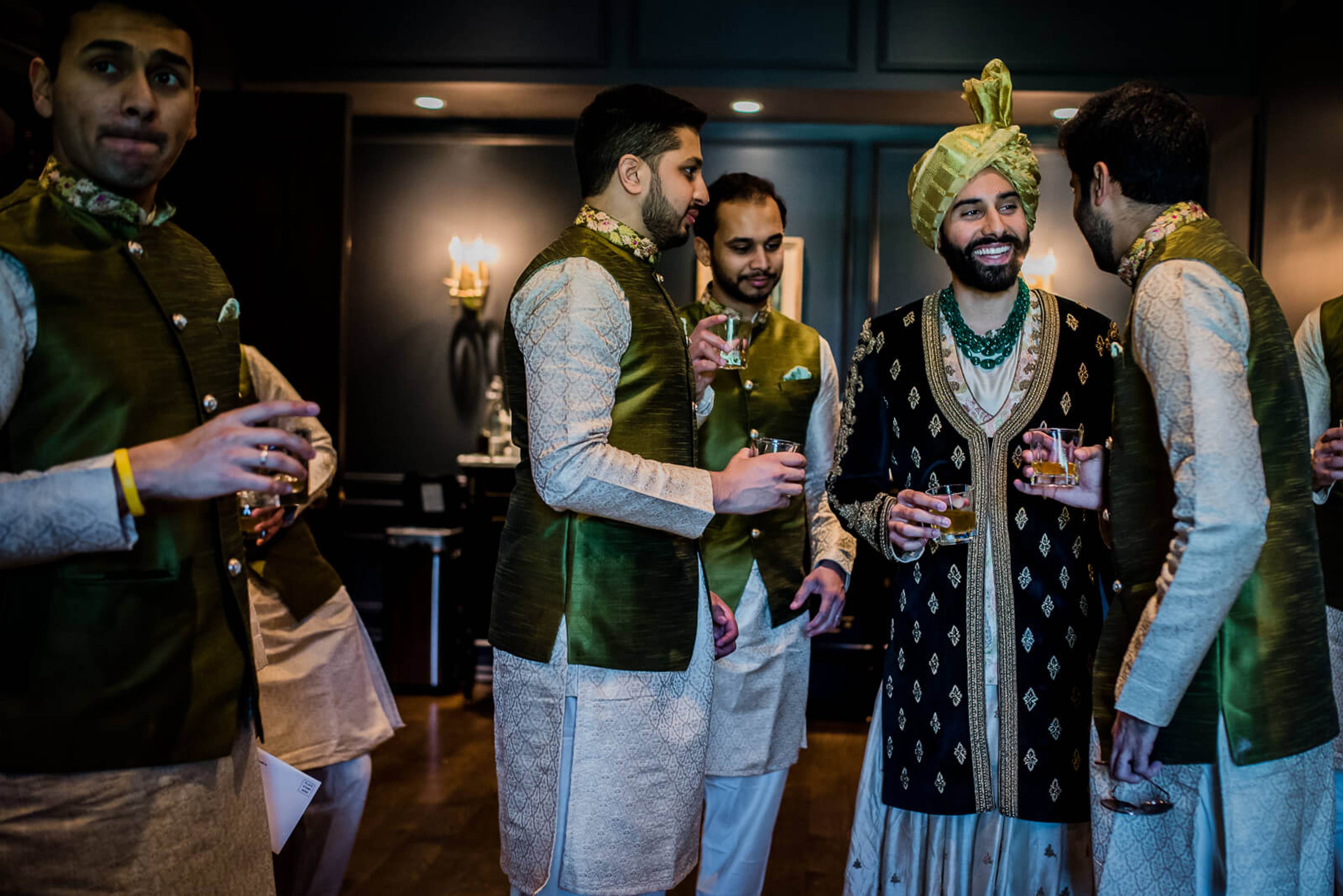 Ankit and groomsmen in traditional gold and green attire celebrate together in New York venue, holding drinks
