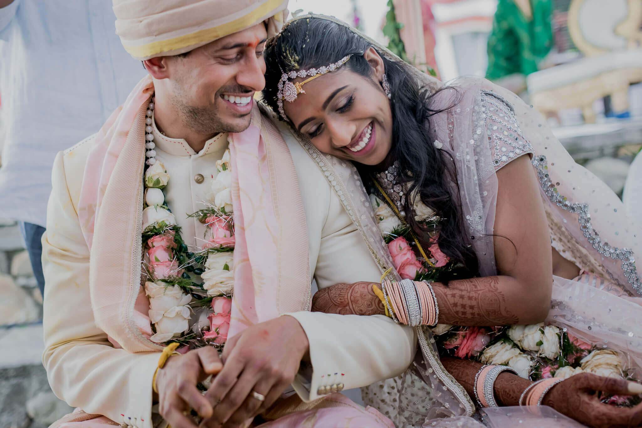 Anu and Raghu smile together in traditional wedding attire with pink and white floral garlands at their Nepal ceremony