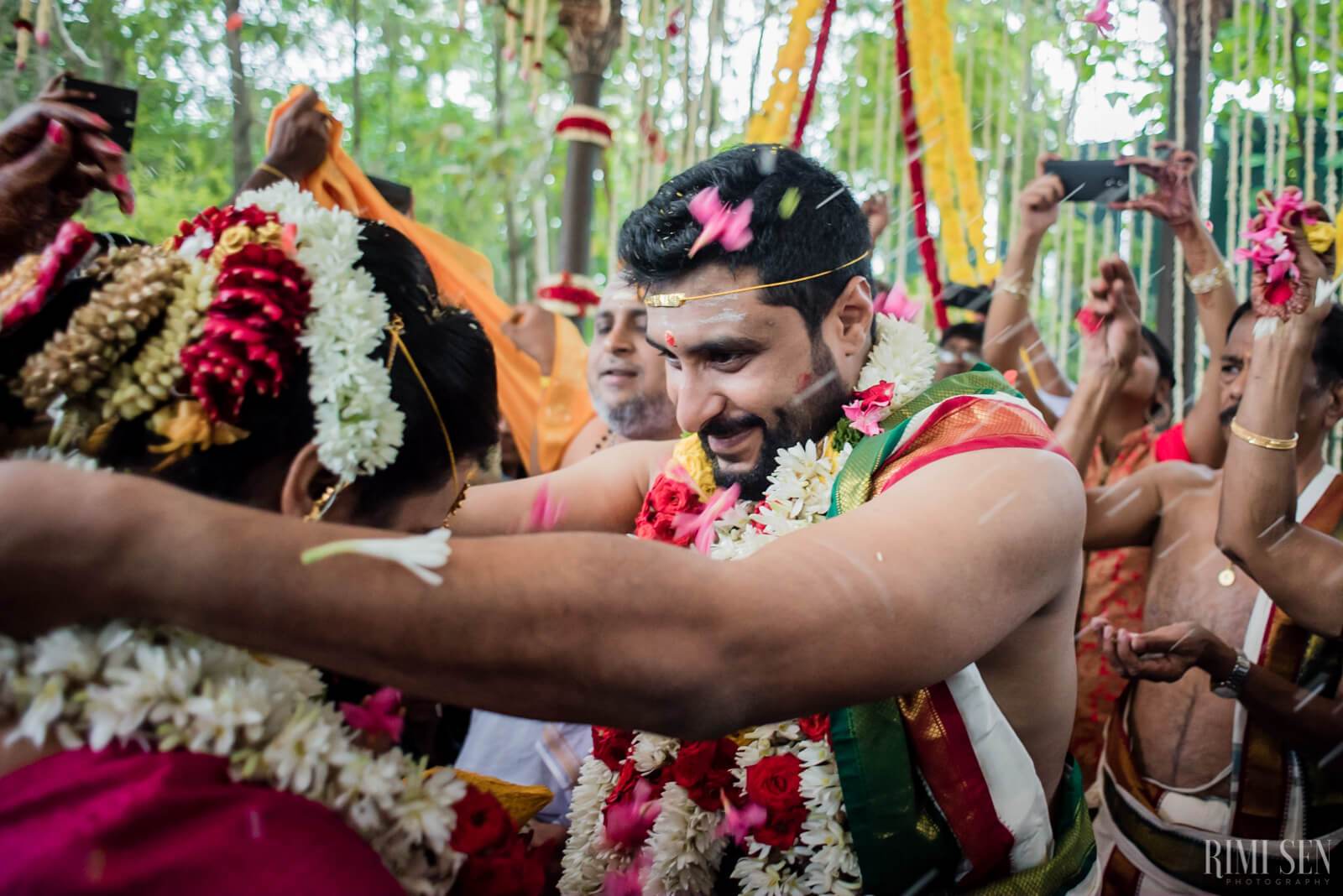 Sridhar wearing traditional attire and floral garlands, smiling among guests in Bangalore wedding celebration