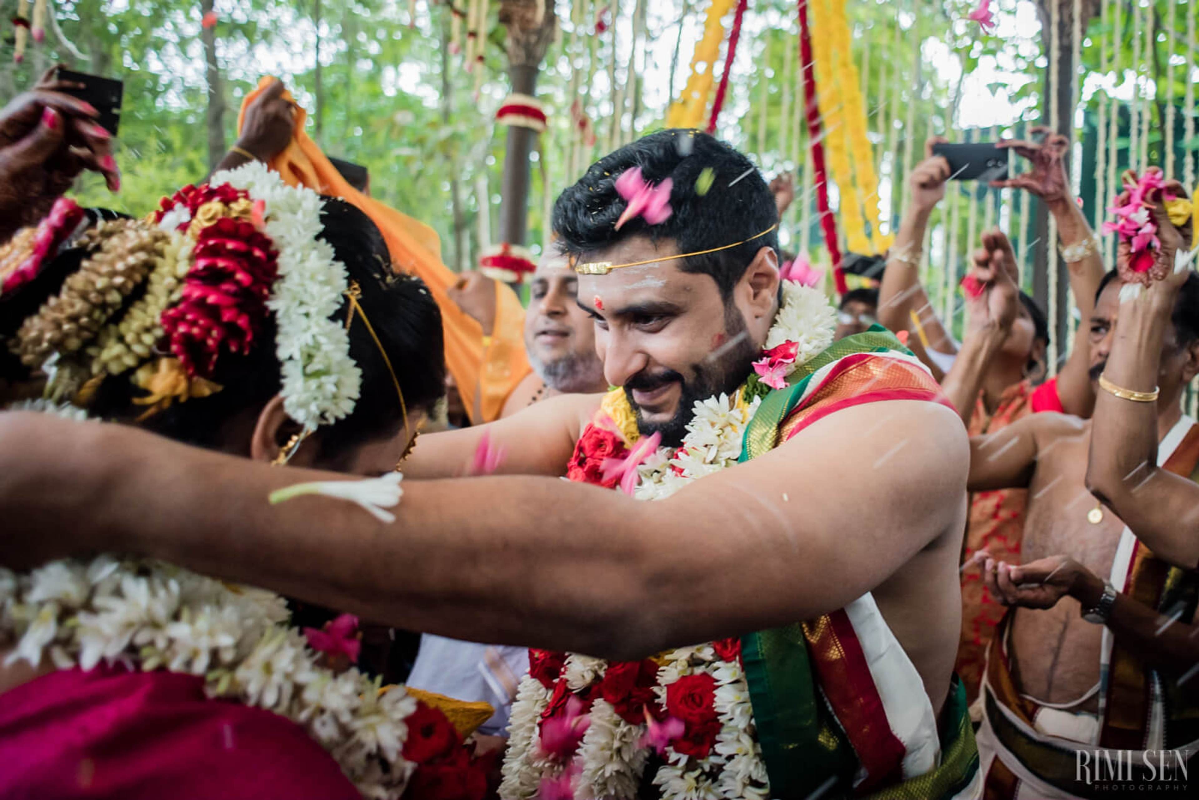 Sridhar wearing traditional attire and floral garlands, smiling among guests in Bangalore wedding celebration