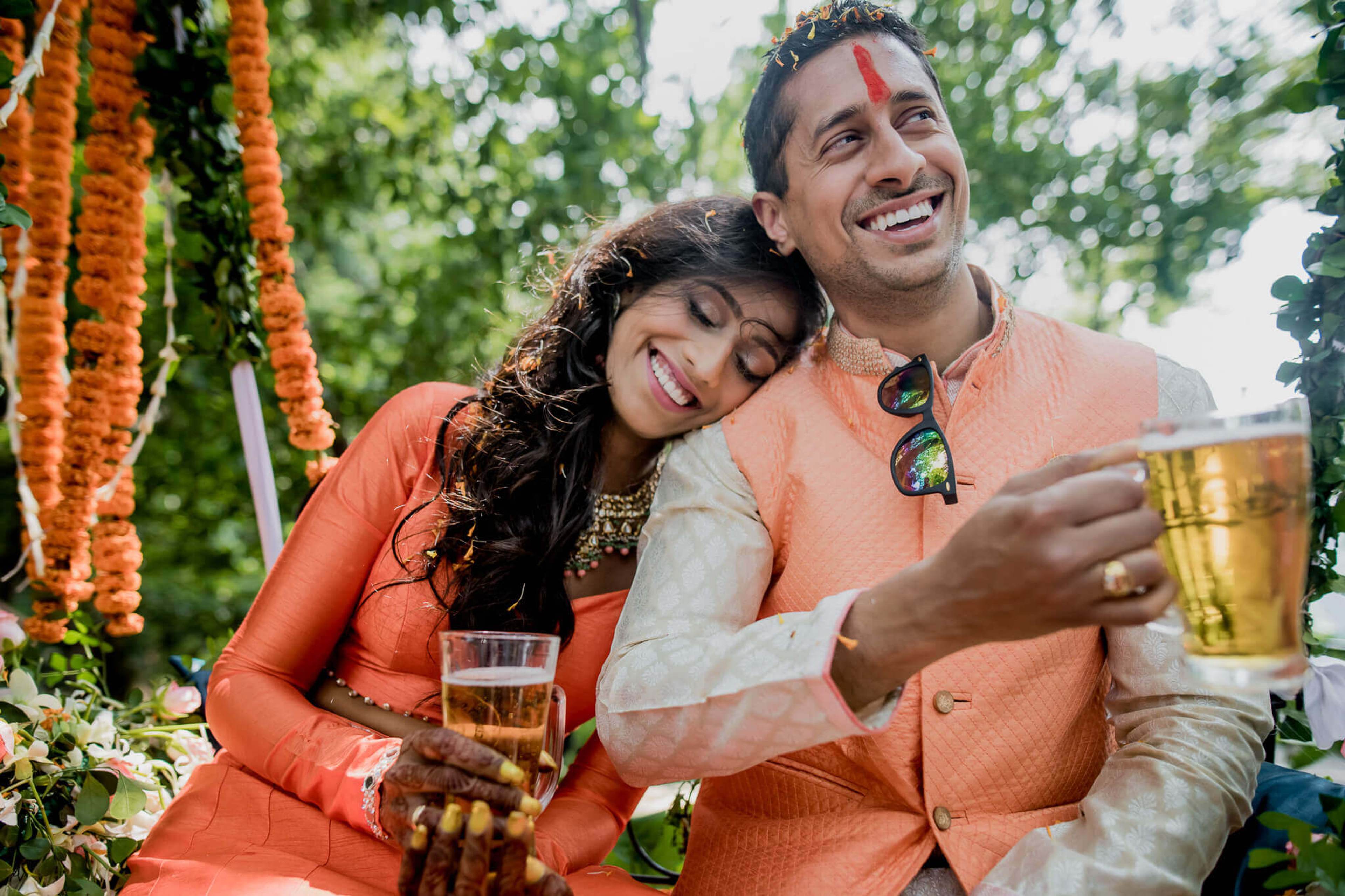 Anu and Raghu smile together under marigold garlands in Nepal, wearing coordinated orange attire at an outdoor celebration
