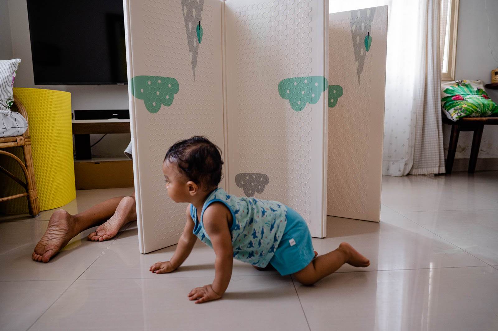 Young child crawling on polished floor near decorative room divider with cloud designs