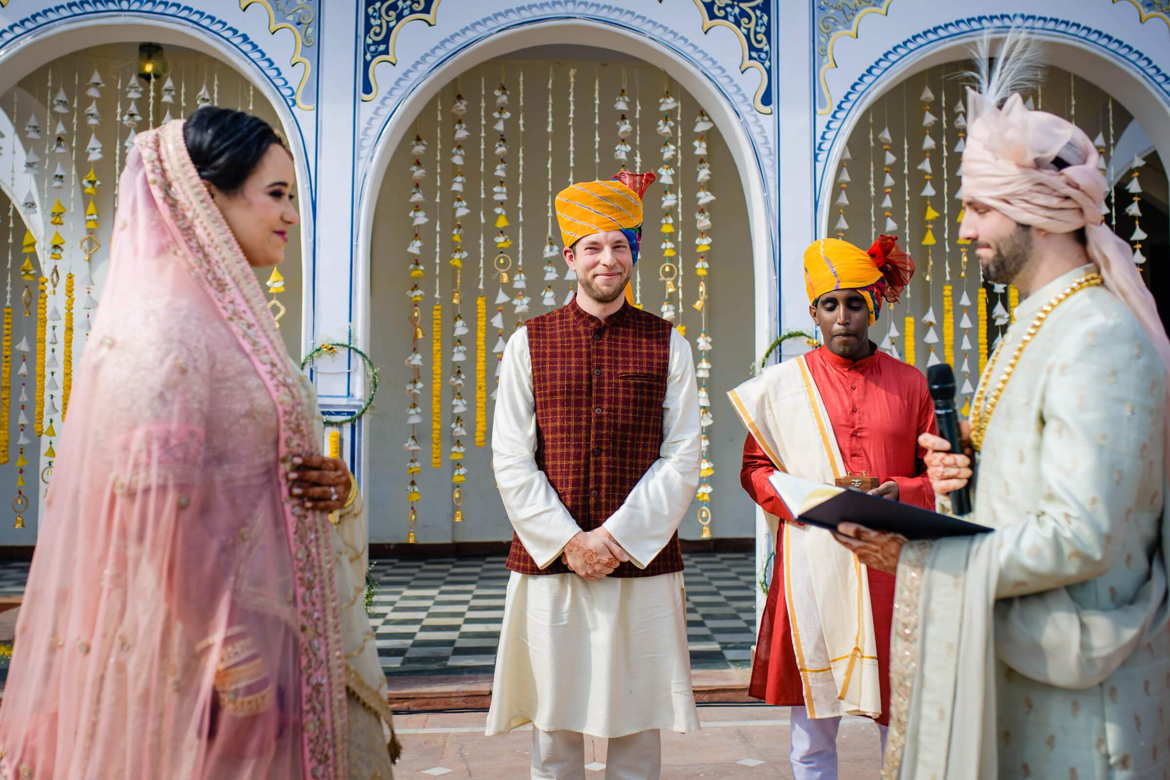 Maitrayee in pink veil and Eric in cream sherwani with officiant during Rajasthani wedding ceremony