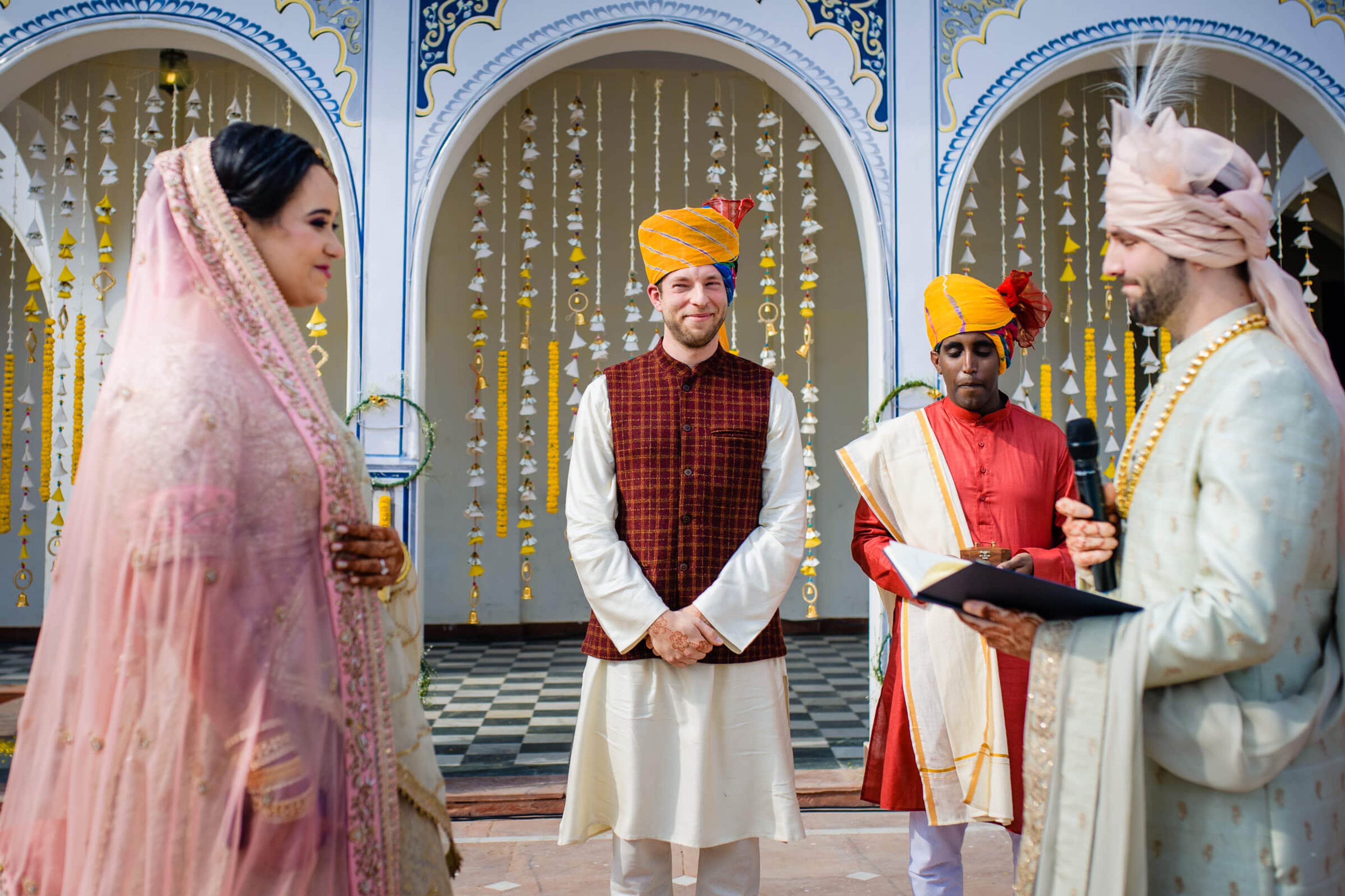 Maitrayee in pink veil and Eric in cream sherwani with officiant during Rajasthani wedding ceremony
