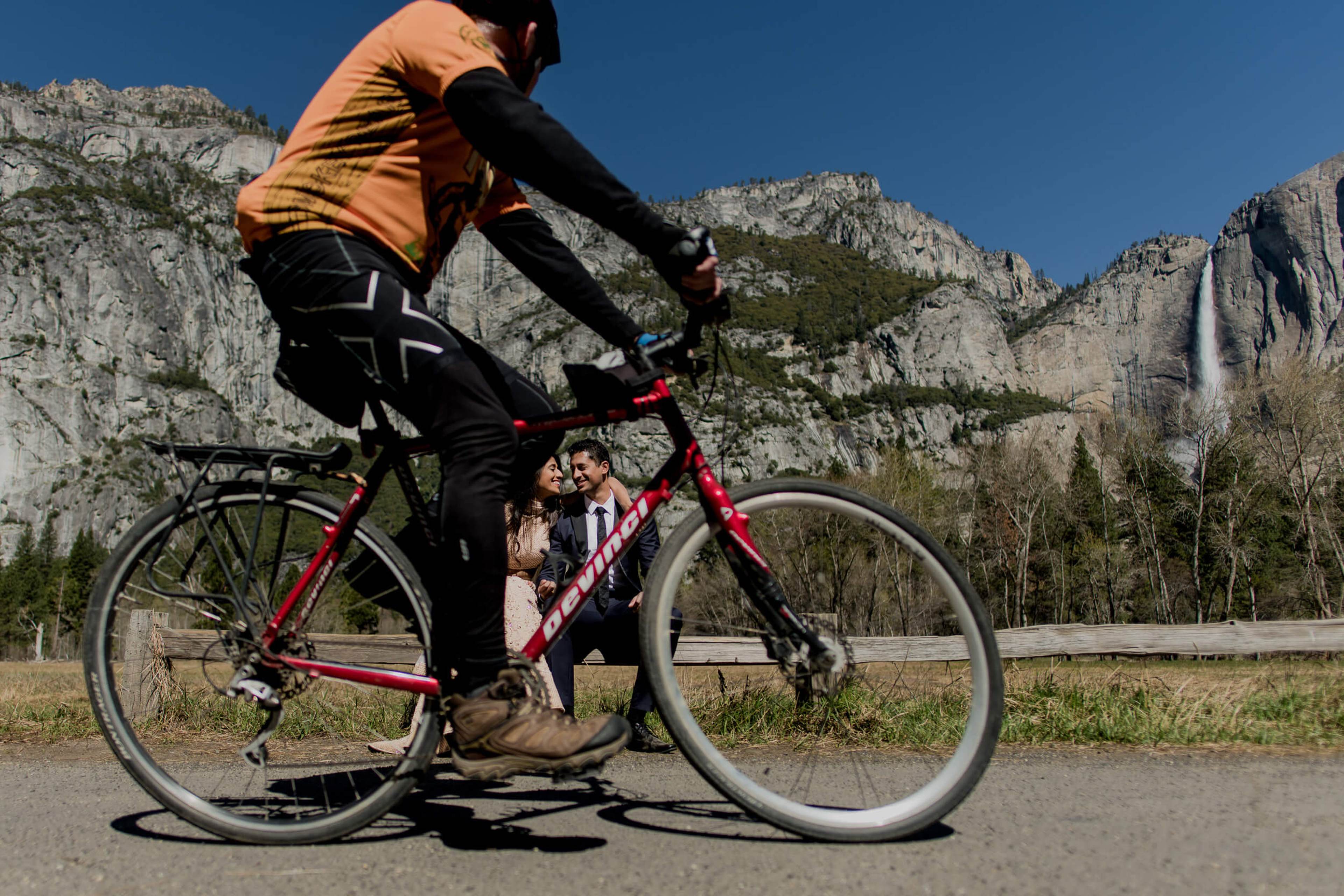 Anu and Raghu cycling on a red bike with granite cliffs and waterfall in California background