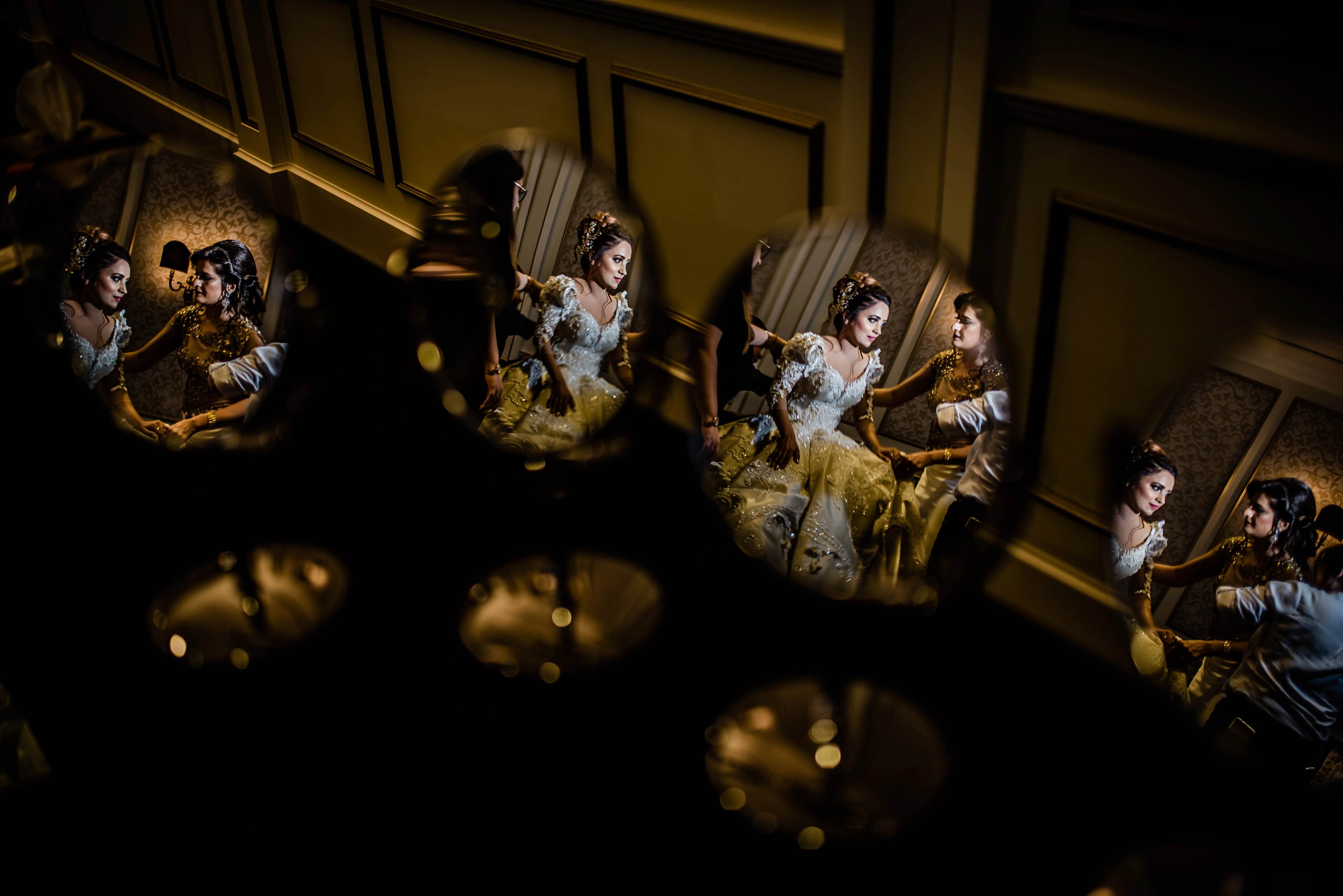 Bride in ornate gold gown reflected multiple times in mirrors, warm light, elegant interior setting