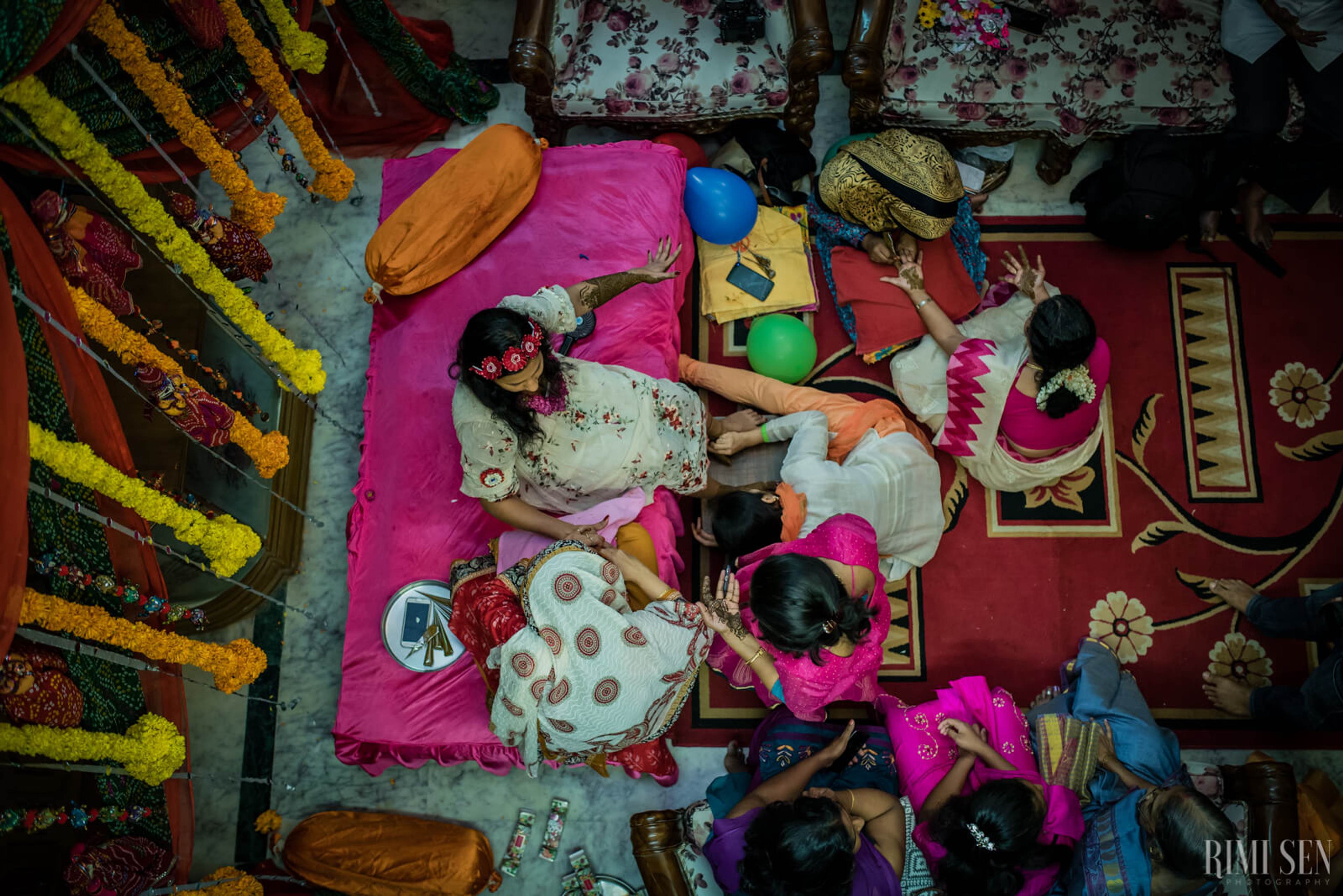 Overhead view of the couple playfully arranged on bright pink bedding surrounded by colorful props and traditional decor in Bangalore