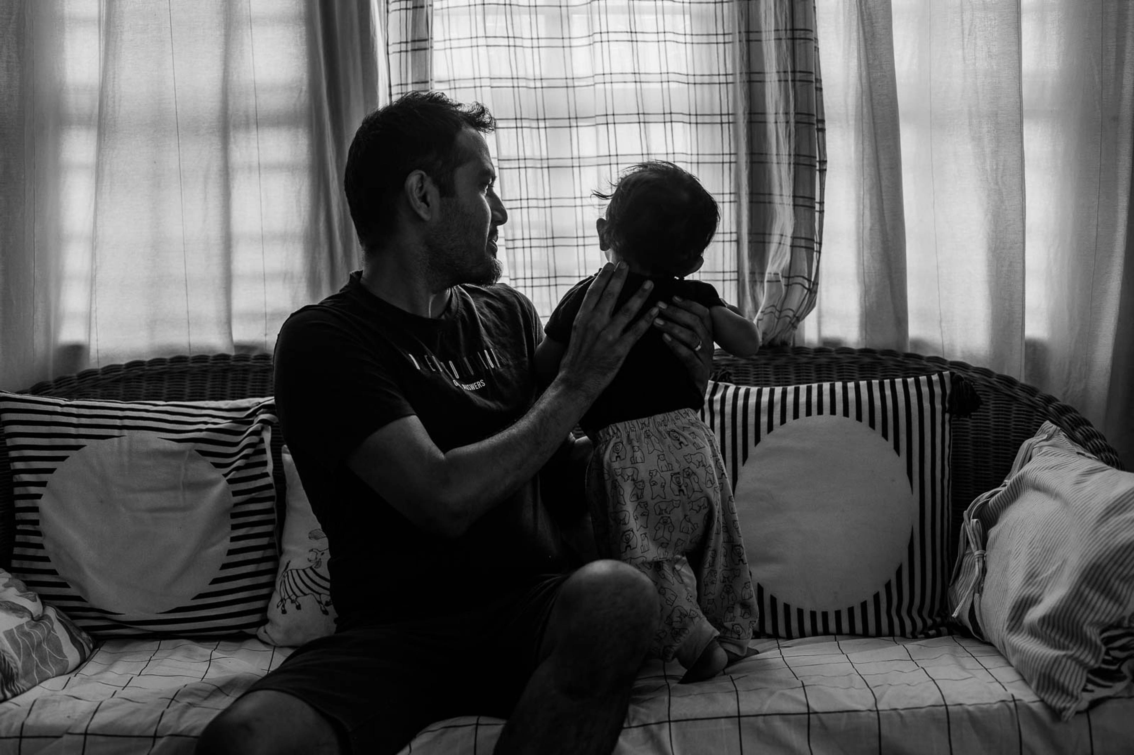 Man and child sitting together on striped sofa by bright window, black and white portrait
