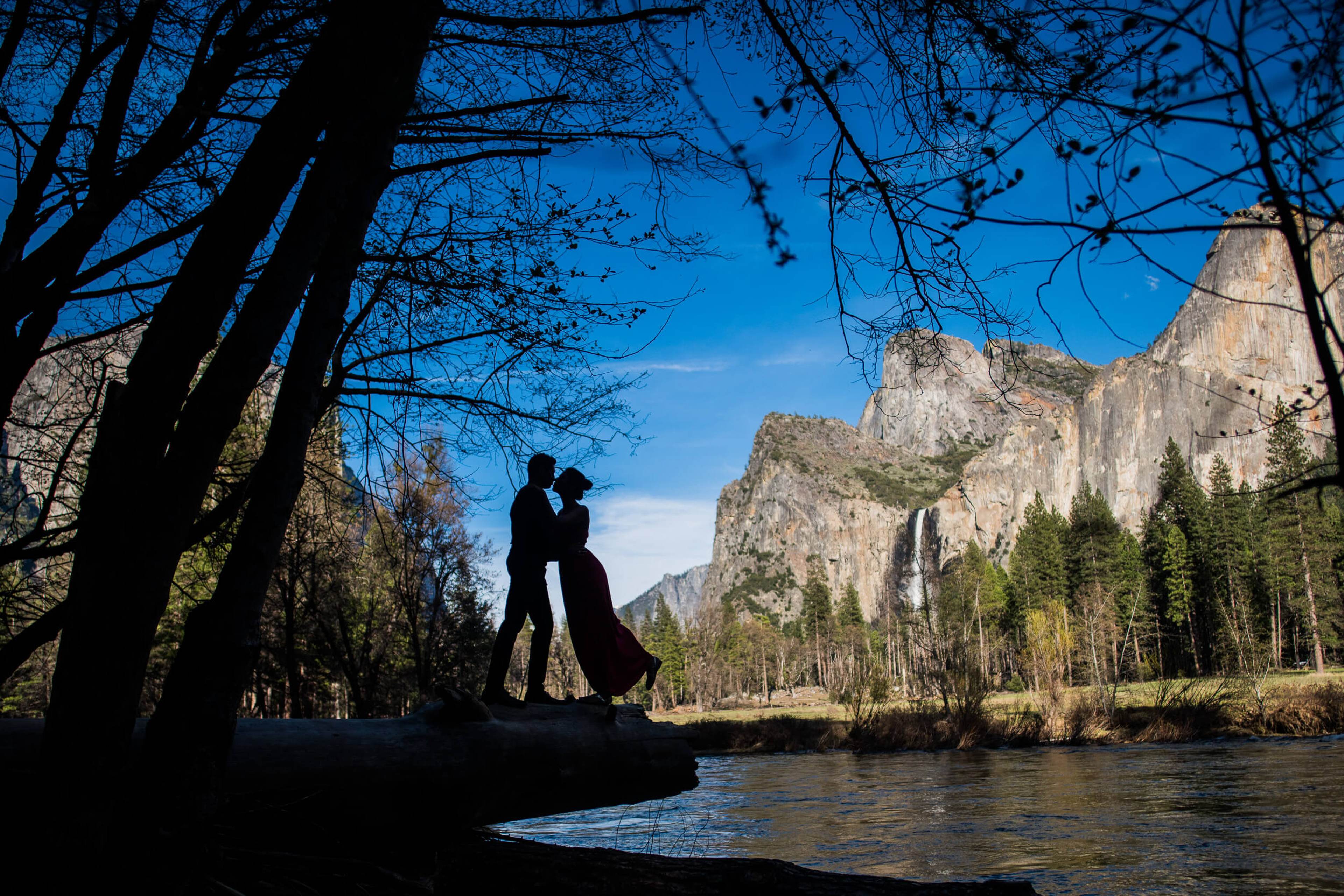 Anu and Raghu embrace by a river under towering granite cliffs in California