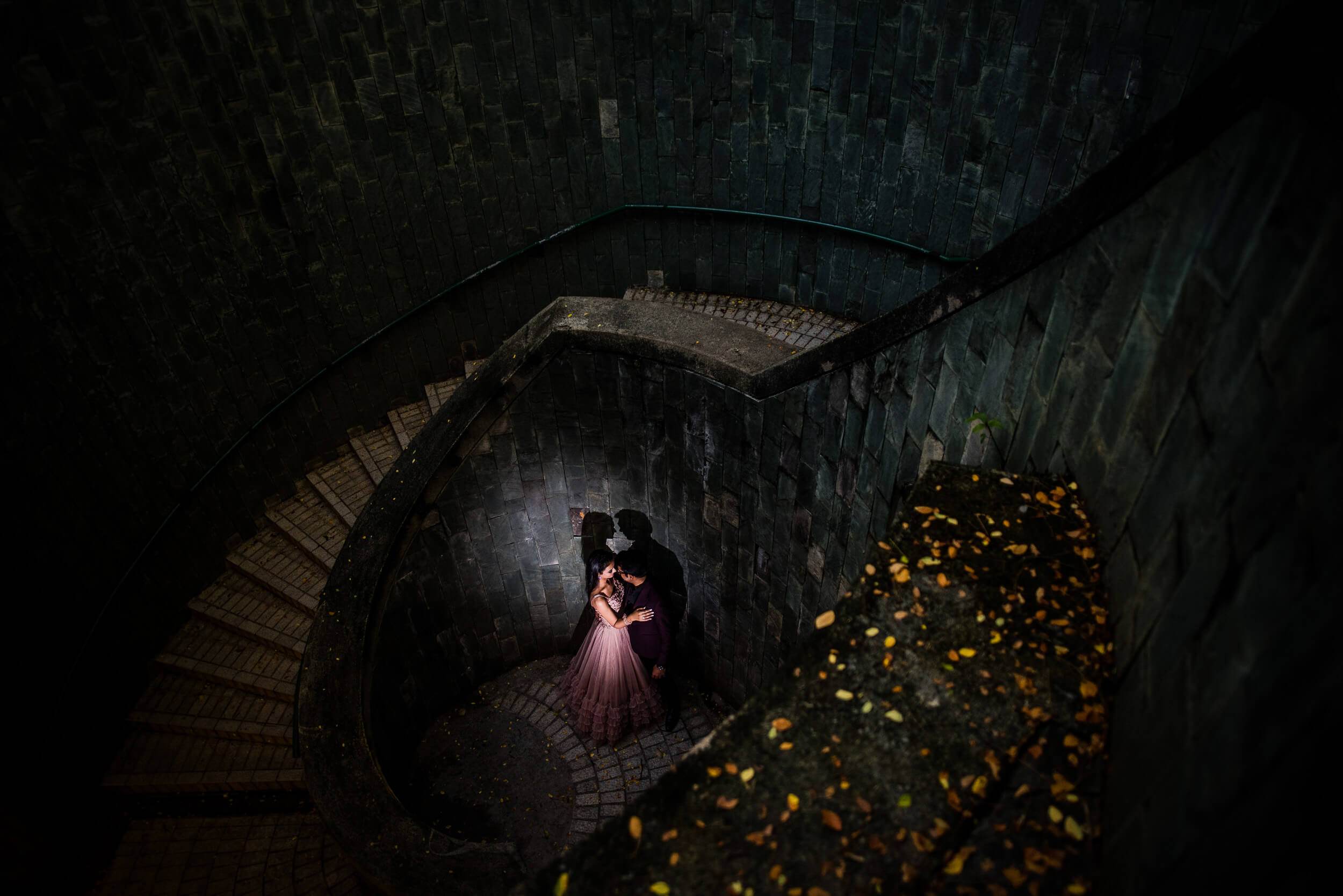 Yash and Disha embrace in a spiral stairwell lit by warm light, golden leaves scattered nearby