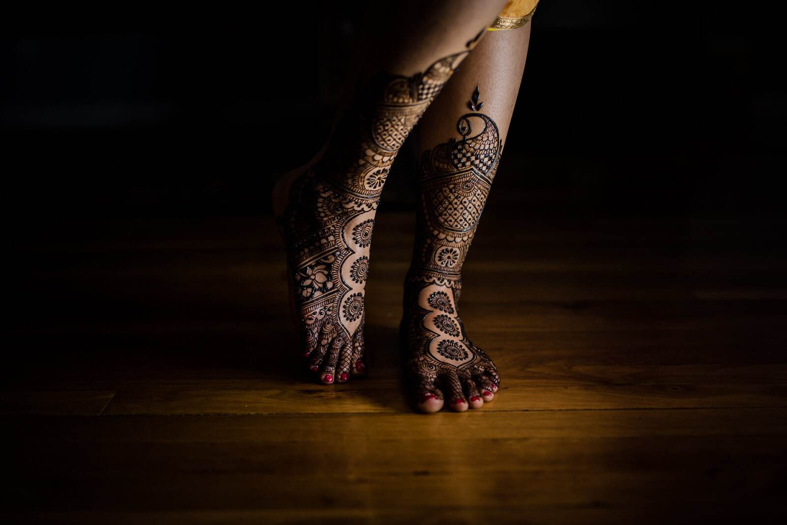Barkha's henna-decorated feet and legs on wooden floor, dramatic warm lighting