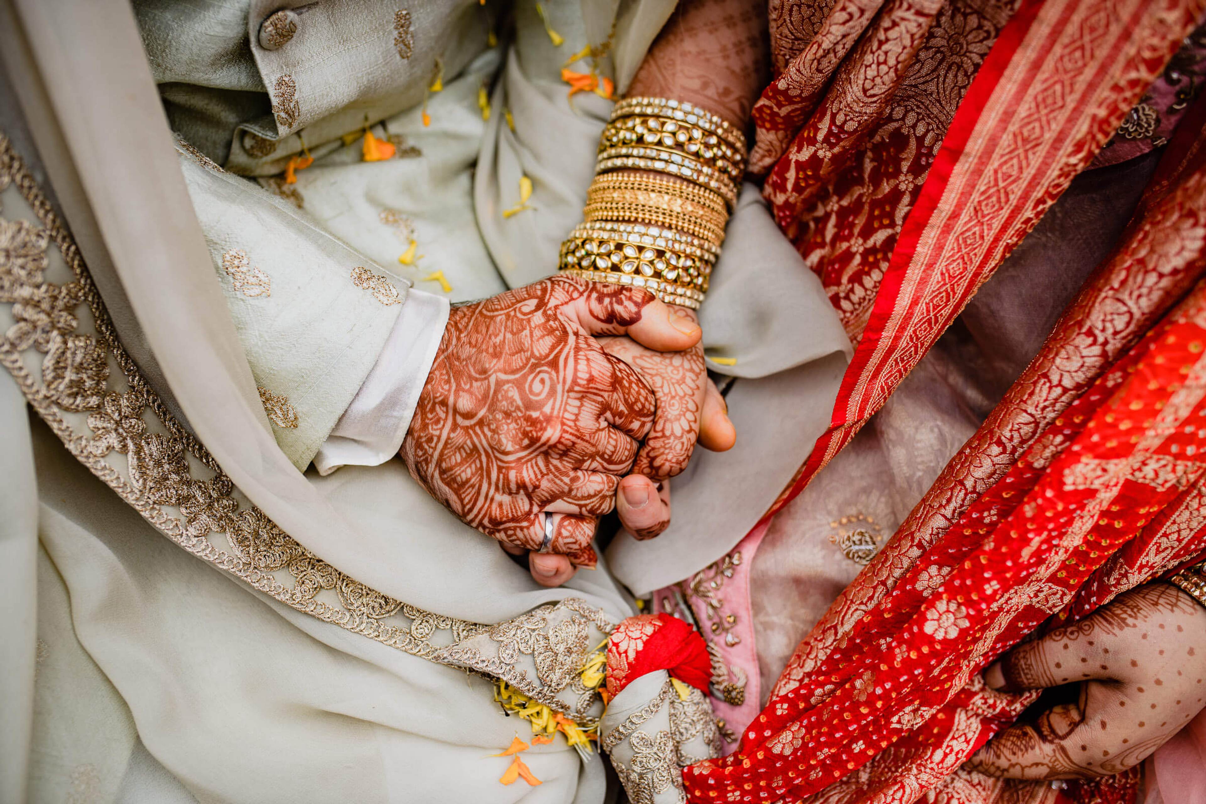 Couple's hands with henna and gold bangles on red and cream wedding attire, Rajasthan ceremony