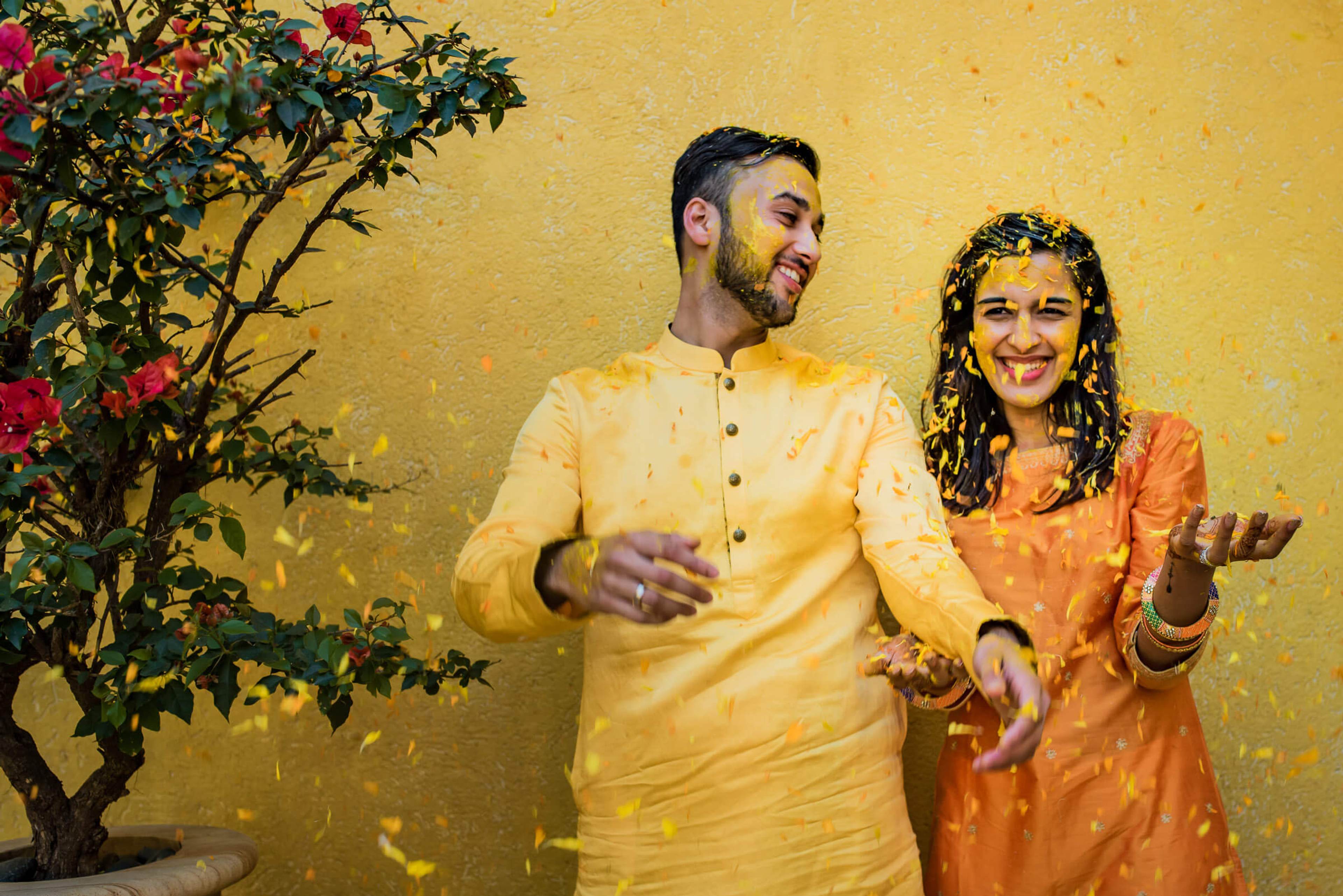 Shreya and Yash celebrate with gold confetti against a yellow wall, wearing traditional attire at Mahabaleshwar