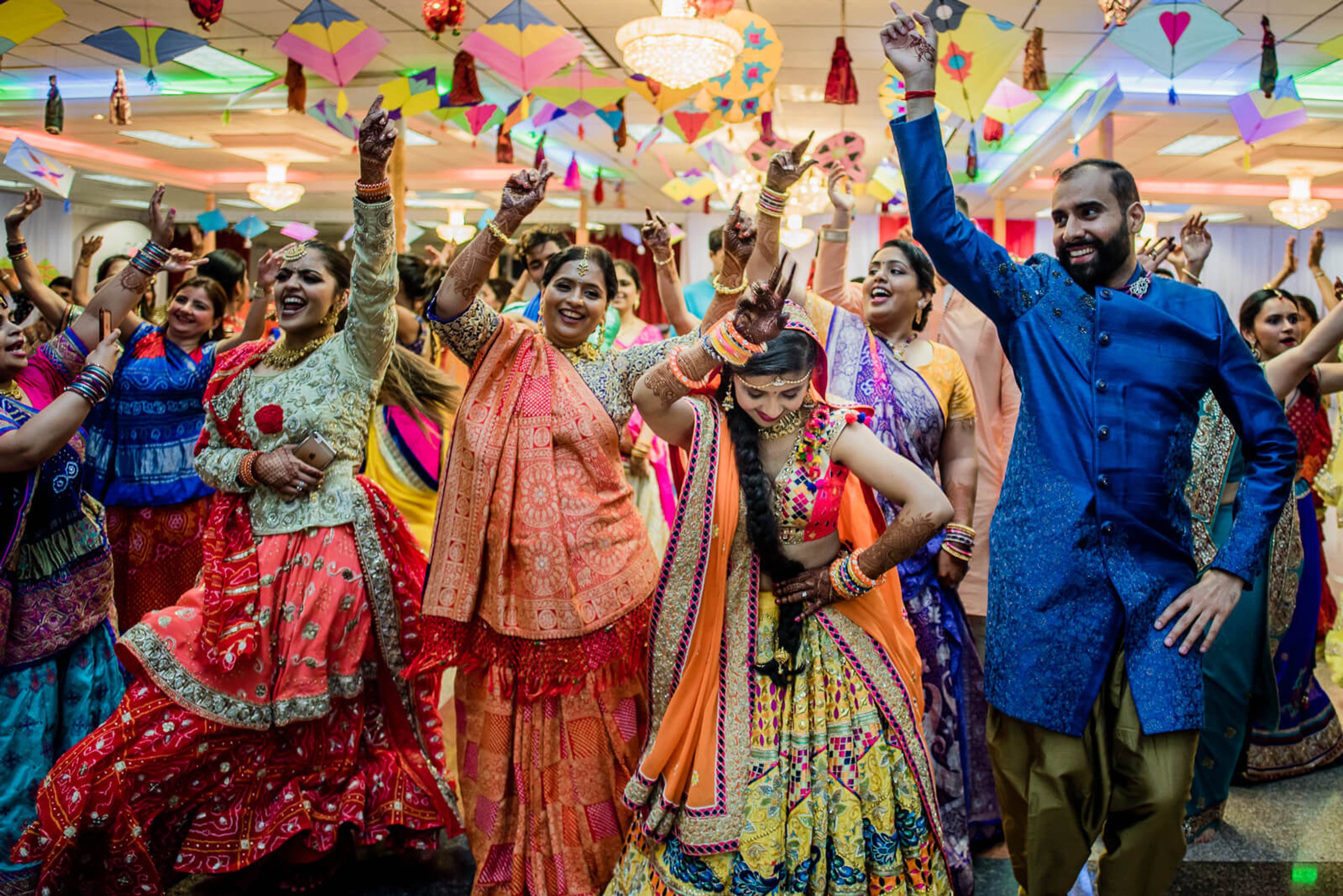 Barkha & Ankit celebrate with joyful guests in colorful traditional attire, arms raised under festive decorations