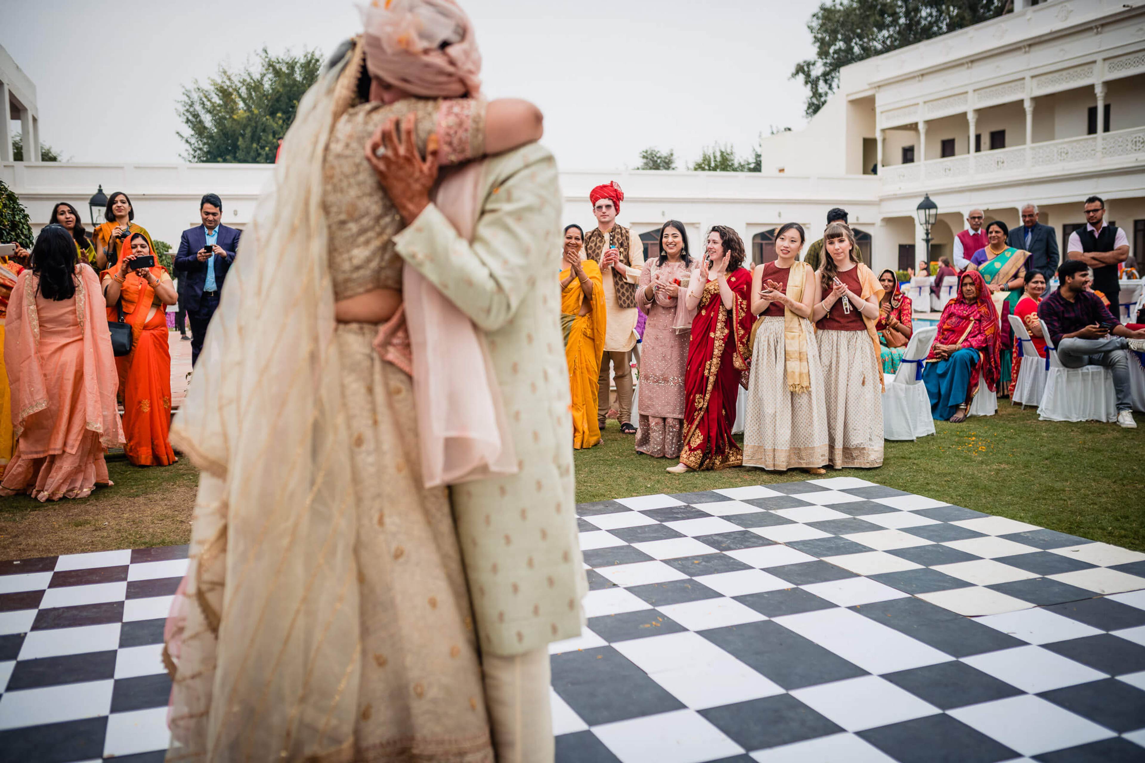 Maitrayee and Eric's groom holds bride aloft during Rajasthan wedding celebration with guests in colorful attire