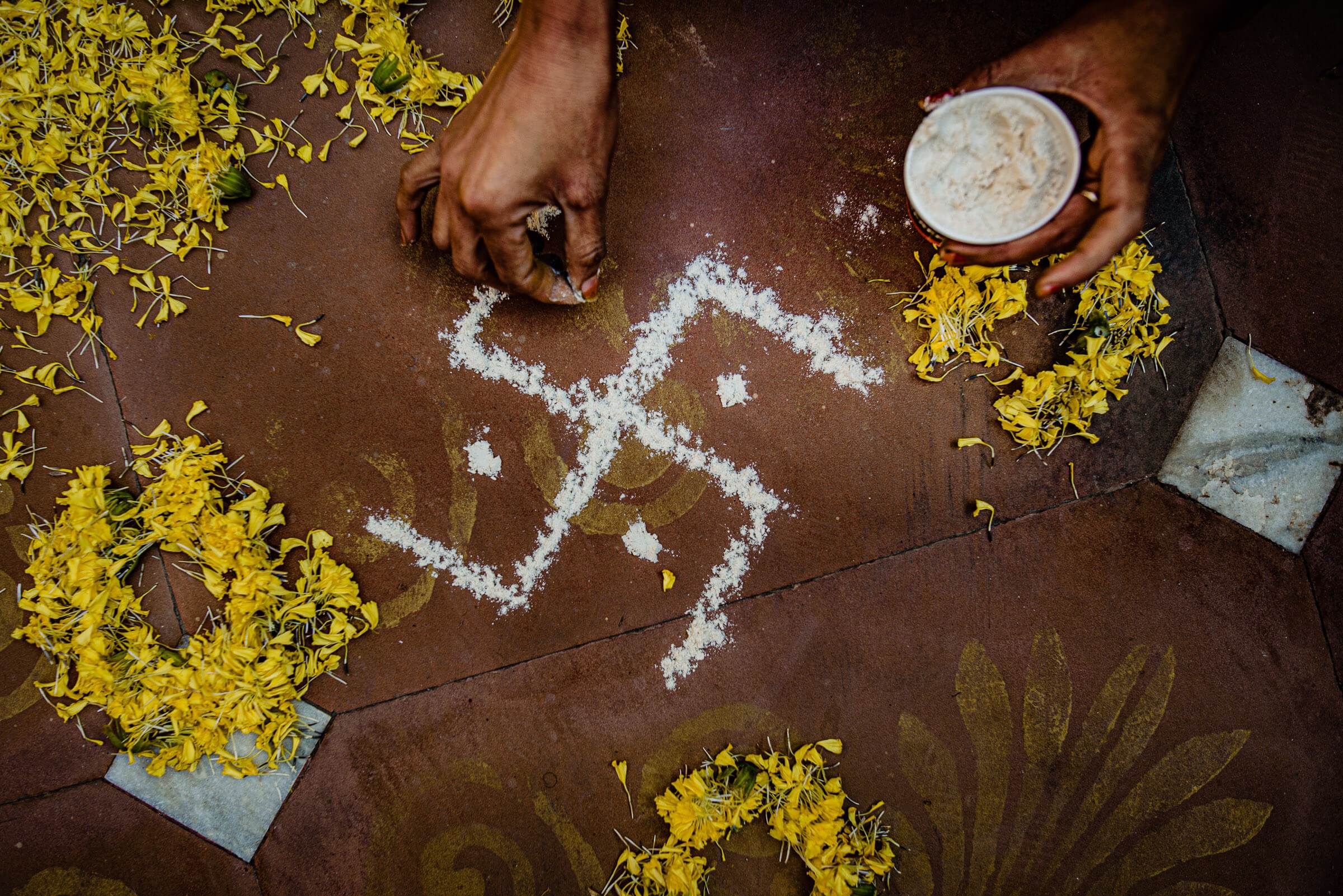 Hands draw rangoli patterns with flour surrounded by yellow flowers in Rajasthan