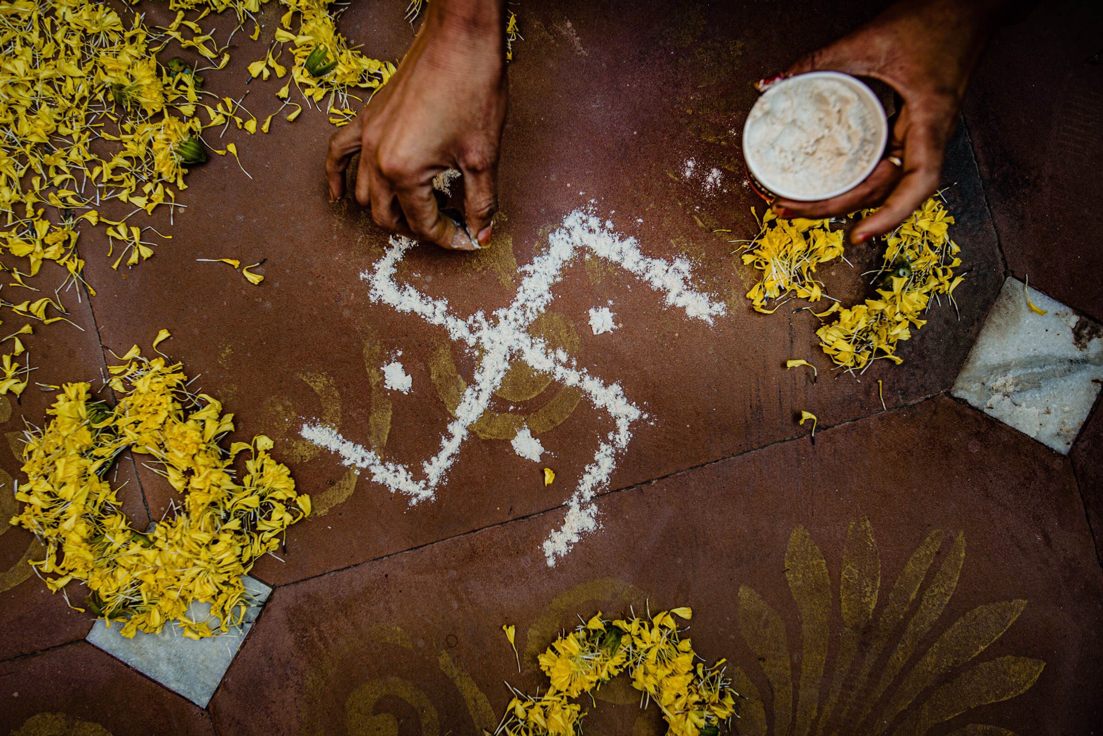 Hands draw rangoli patterns with flour surrounded by yellow flowers in Rajasthan
