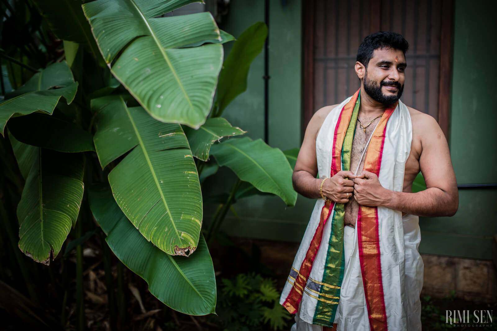 Sridhar stands by lush banana leaves in traditional attire, holding a colorful fabric shawl