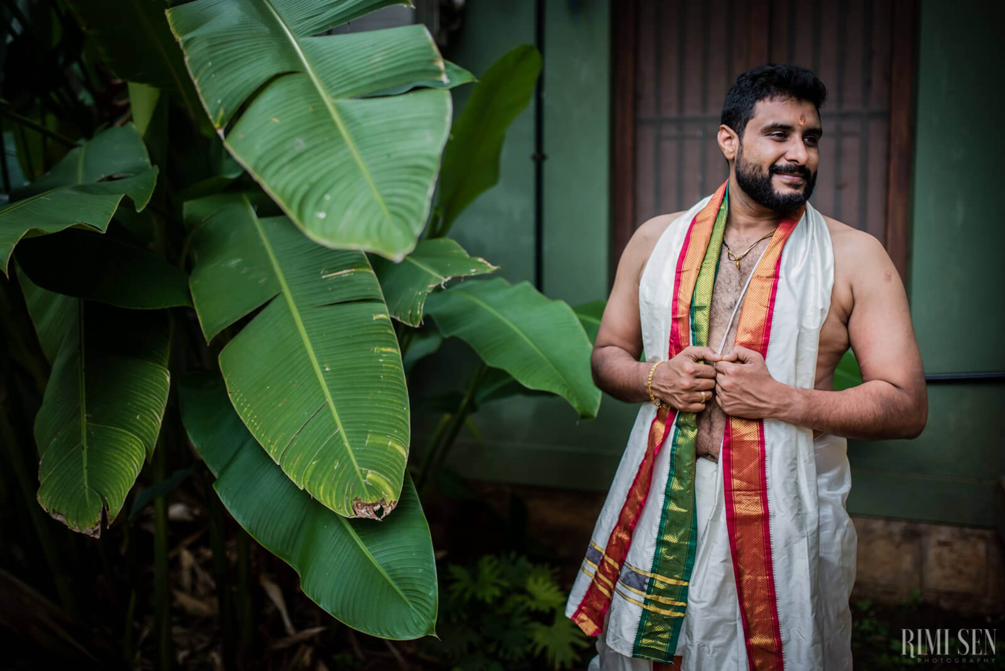 Sridhar stands by lush banana leaves in traditional attire, holding a colorful fabric shawl