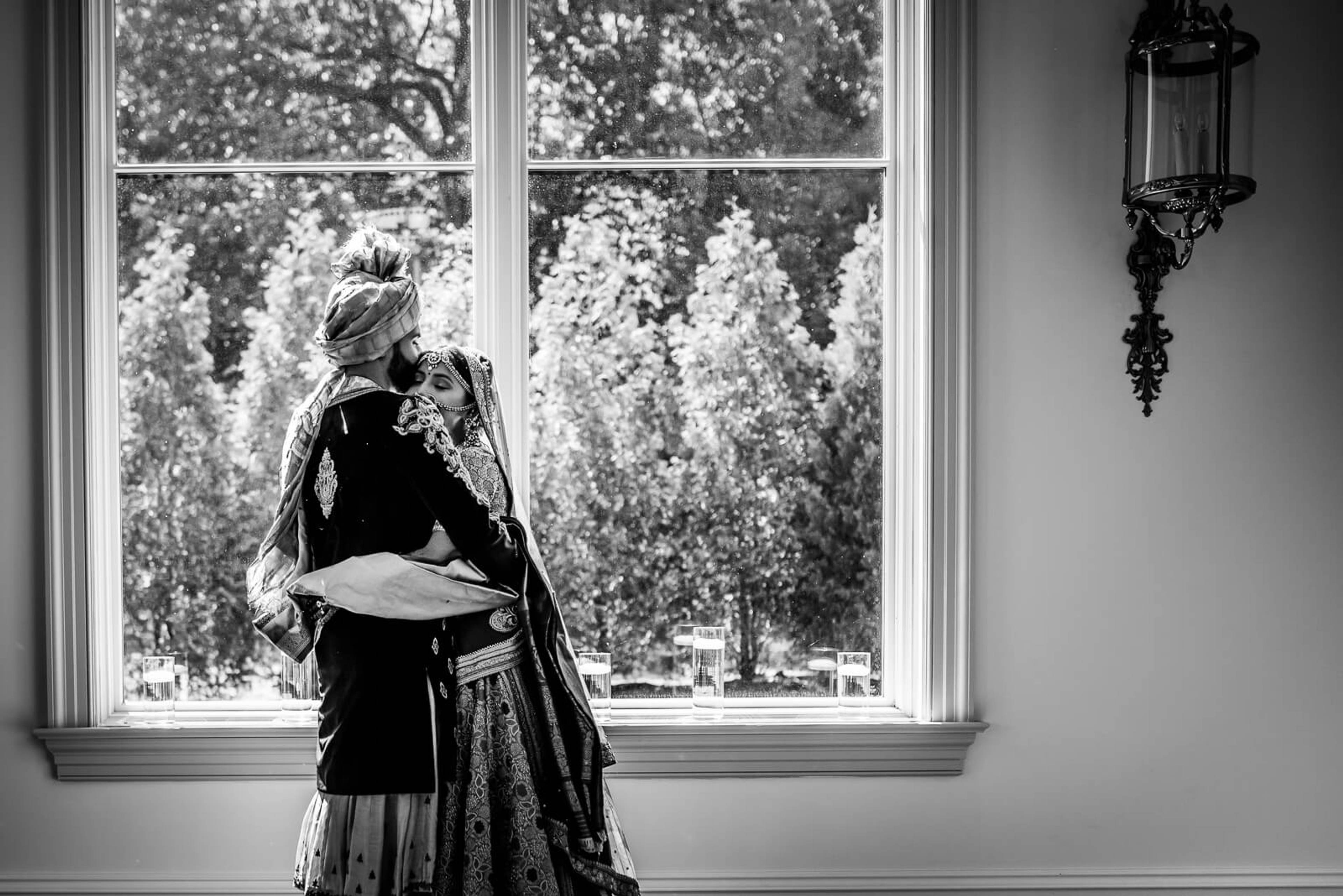 Barkha gazes out tall windows toward lush trees, wearing an ornate shawl in black and white