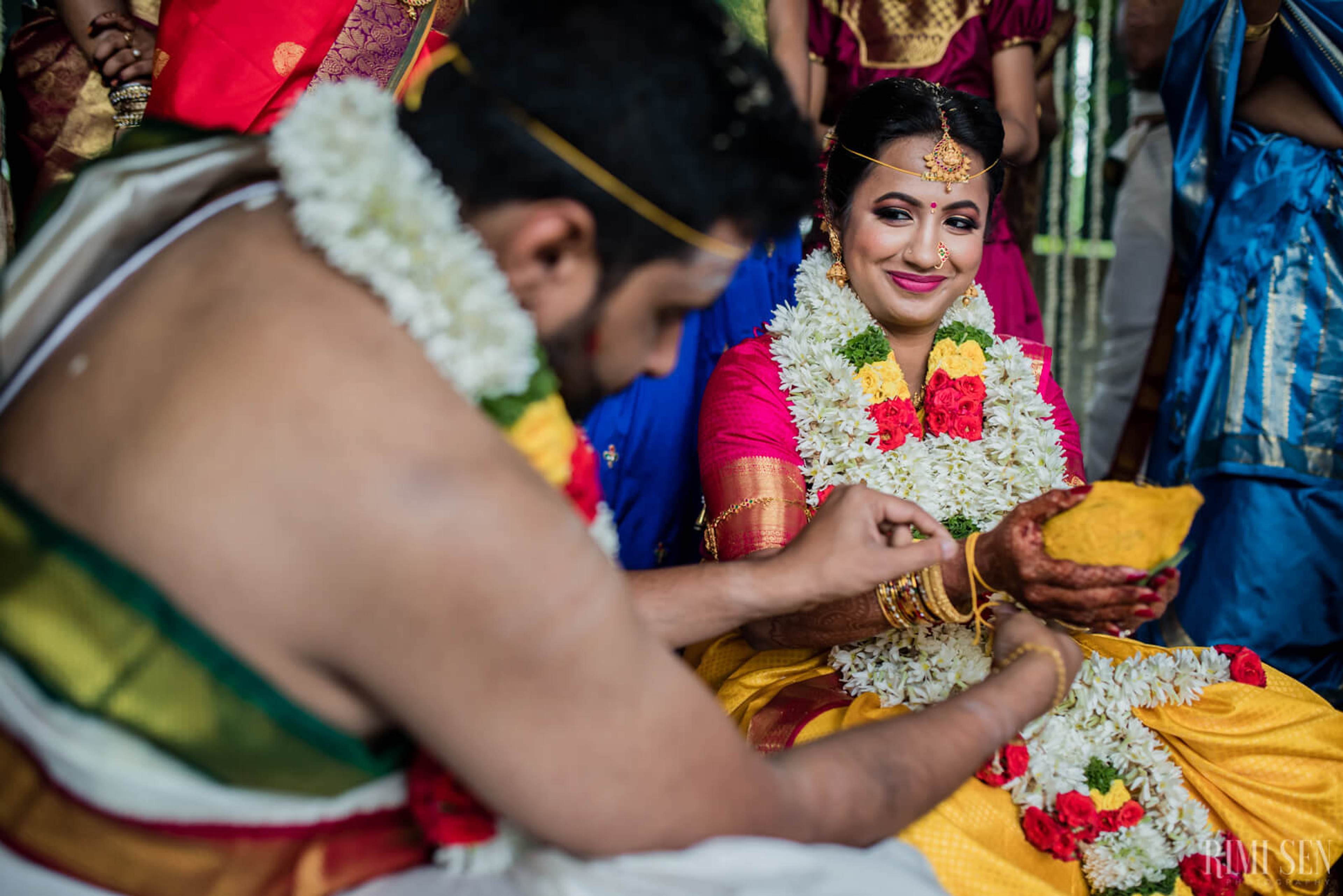 Nivetha smiles while wearing a white and red flower garland during a Bangalore wedding ceremony ritual