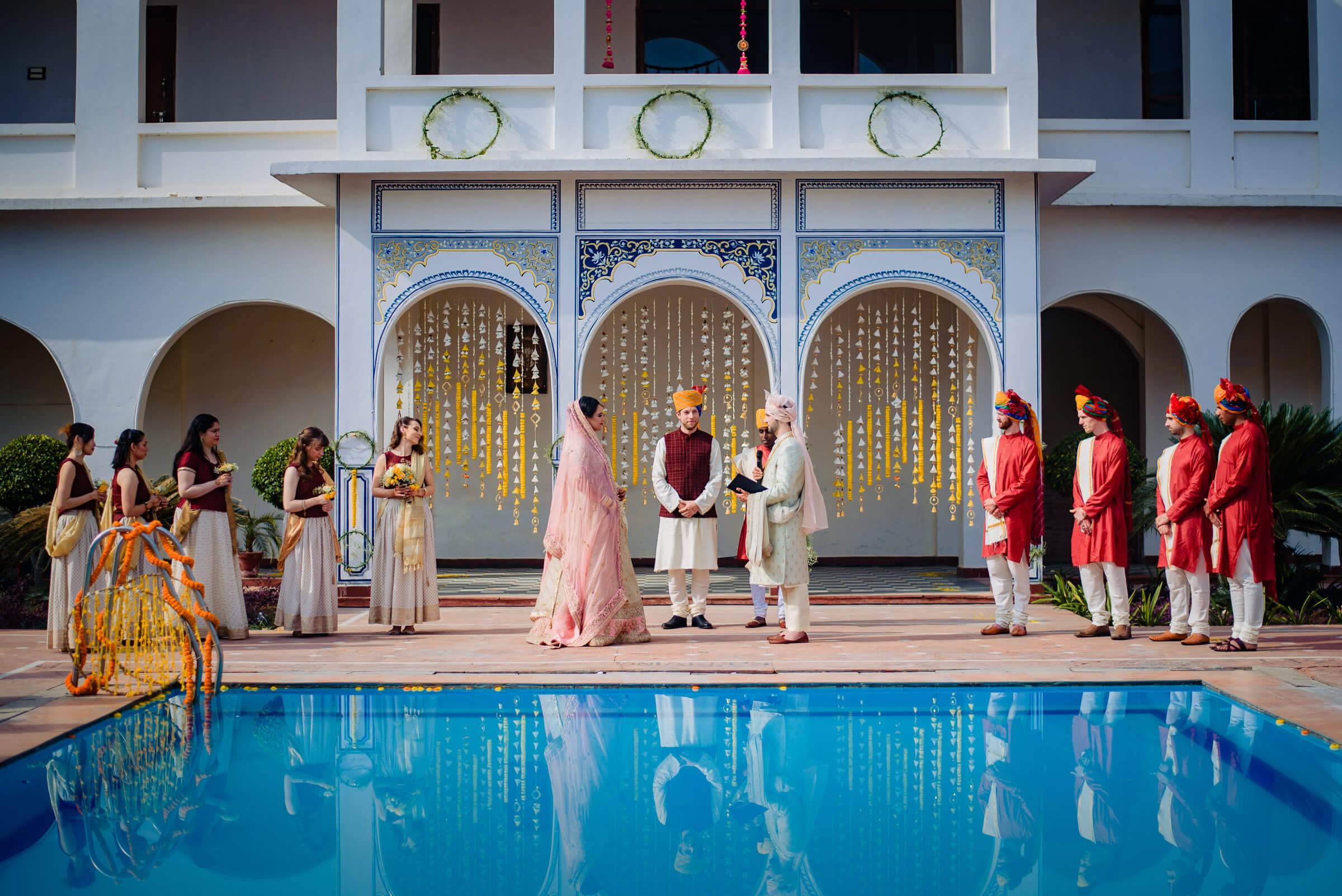 Maitrayee and Eric's wedding ceremony in Rajasthan, guests in traditional attire by ornate doors and pool