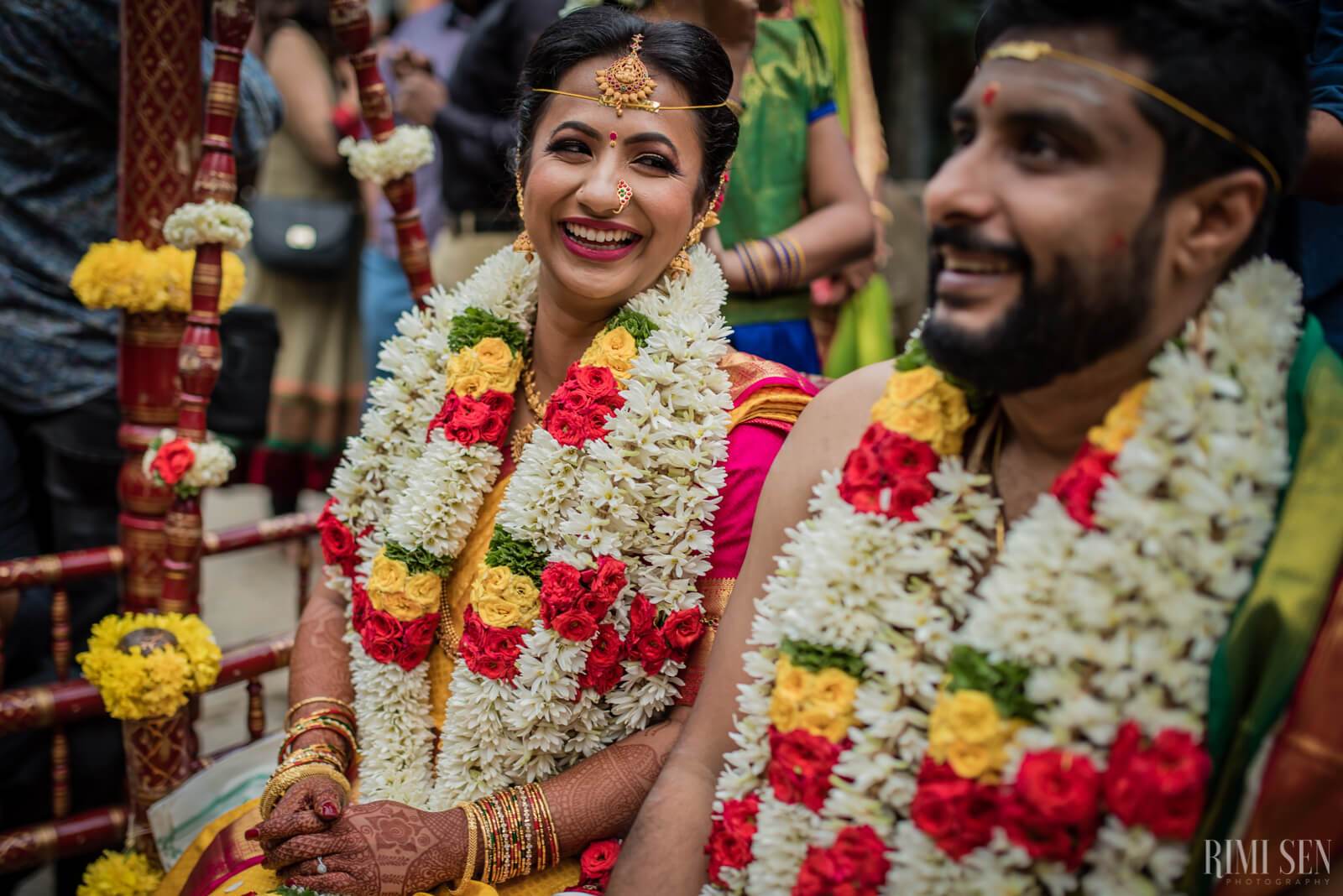 Nivetha and Sridhar exchange smiles during traditional wedding ceremony with colorful flower garlands
