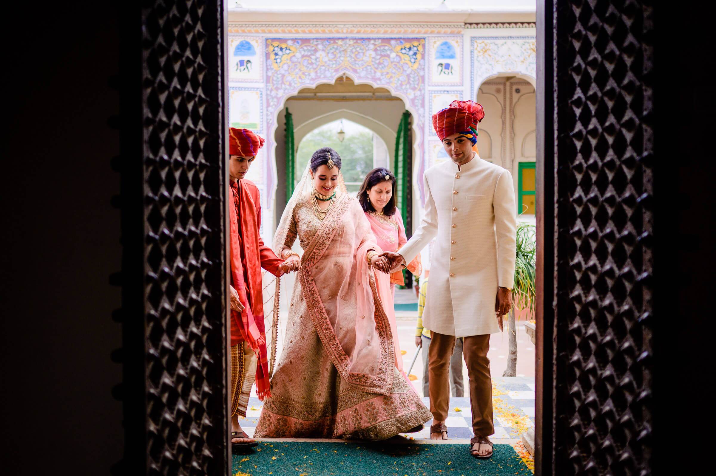 Maitrayee and Eric in traditional wedding attire at ornate Rajasthan palace doorway with family members