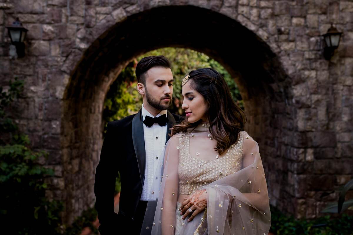 Shreya and Yash stand framed under a stone arch, dressed formally in evening attire at Mahabaleshwar