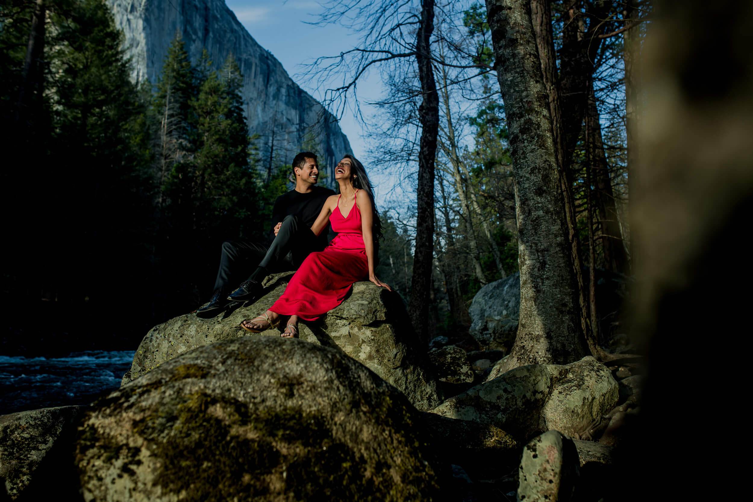 Anu and Raghu sit on a mossy boulder by a stream, surrounded by tall trees and granite cliffs in California by Rimi Sen
