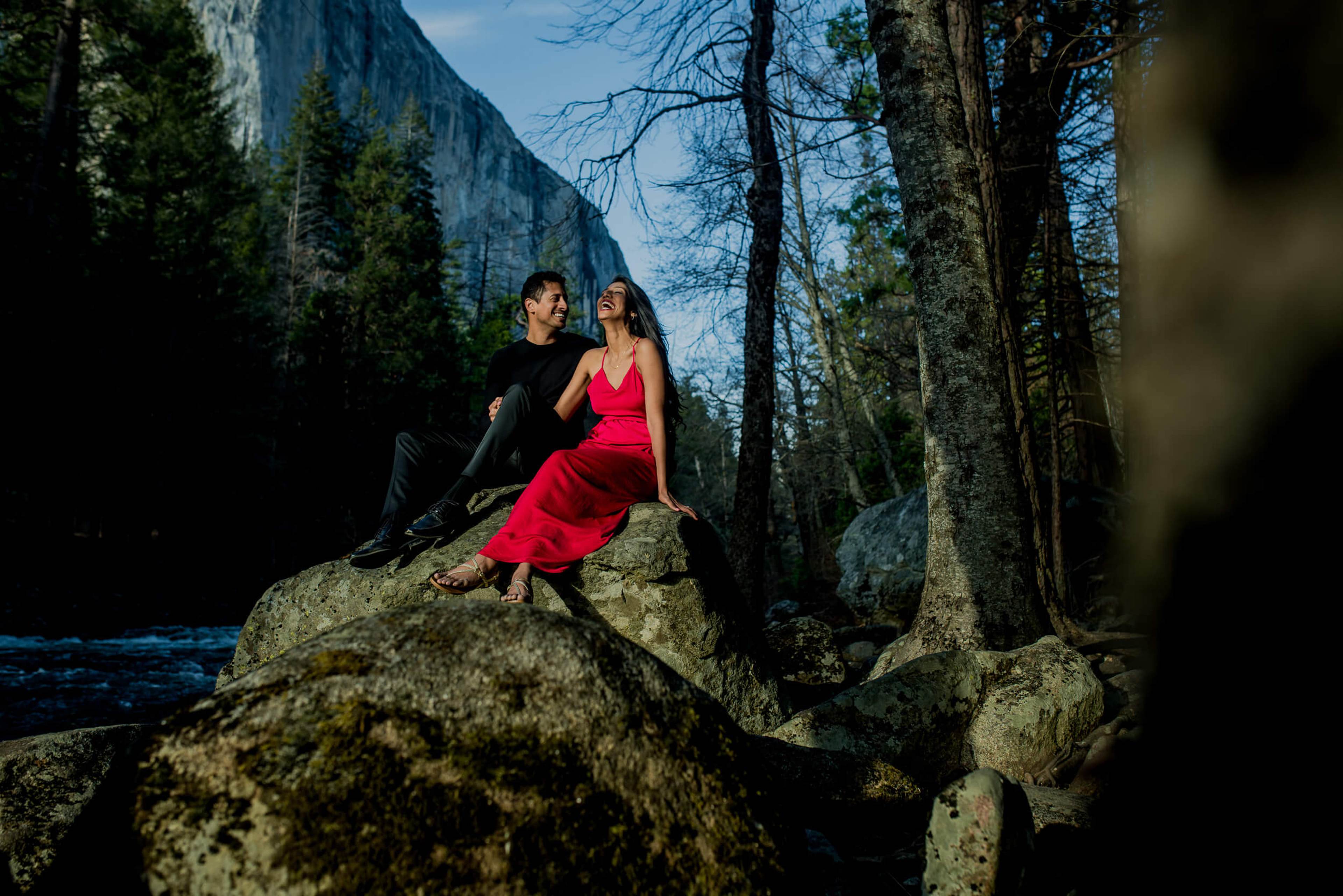 Anu and Raghu sit on a mossy boulder by a stream, surrounded by tall trees and granite cliffs in California by Rimi Sen