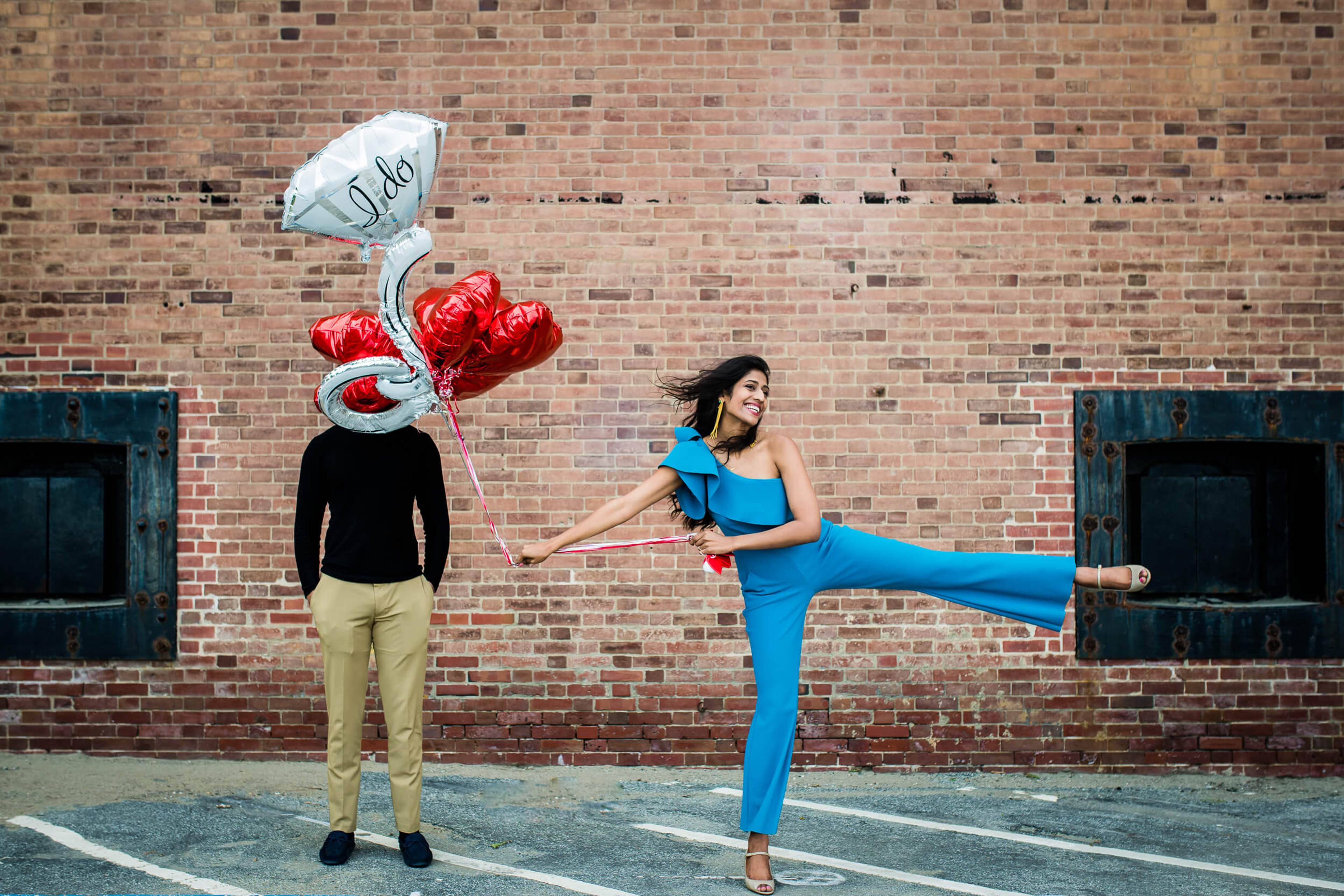 Anu and Raghu pose playfully against a red brick wall with heart-shaped balloons in California