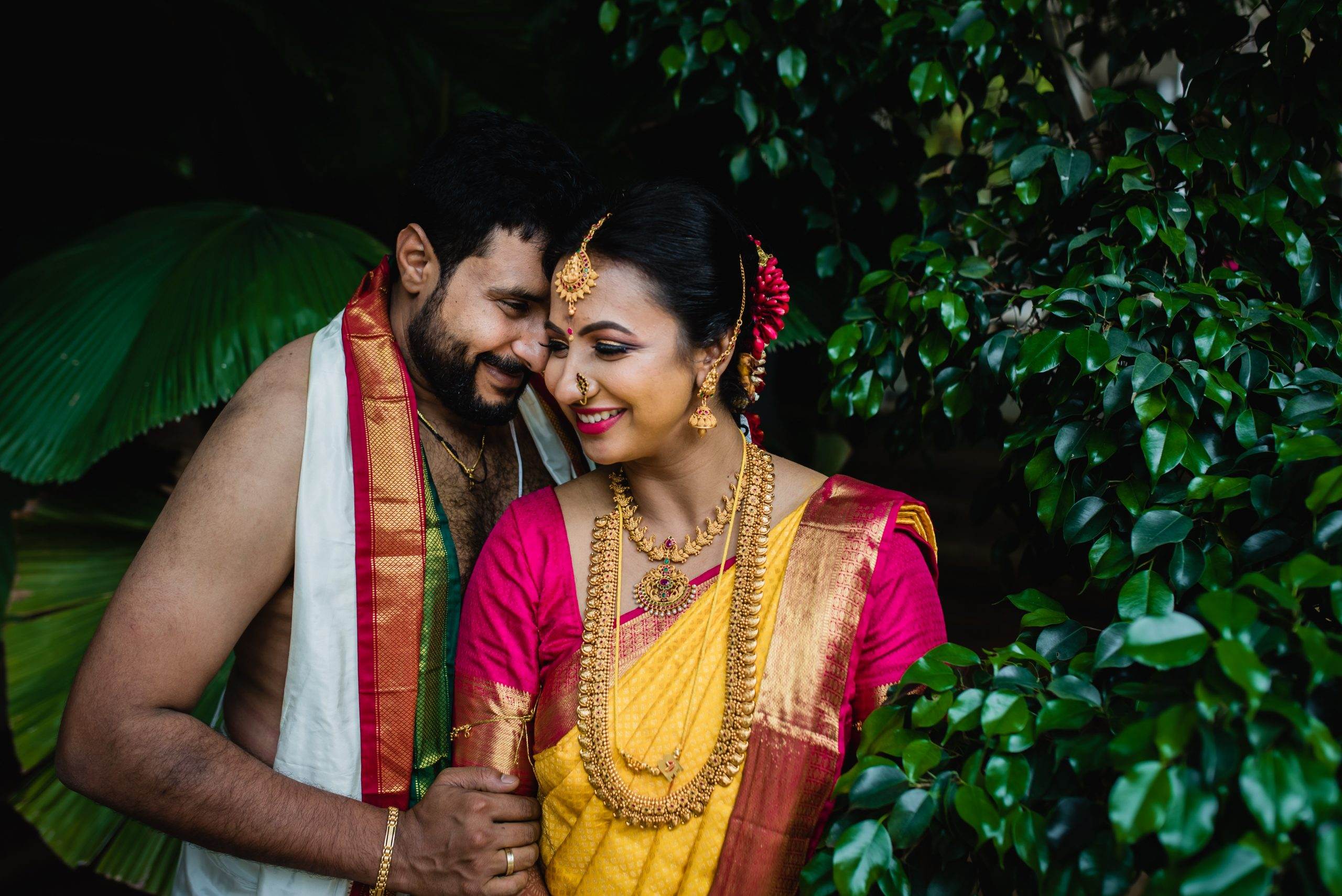 Bride and groom in traditional South Indian wedding attire sharing a quiet moment amid lush greenery