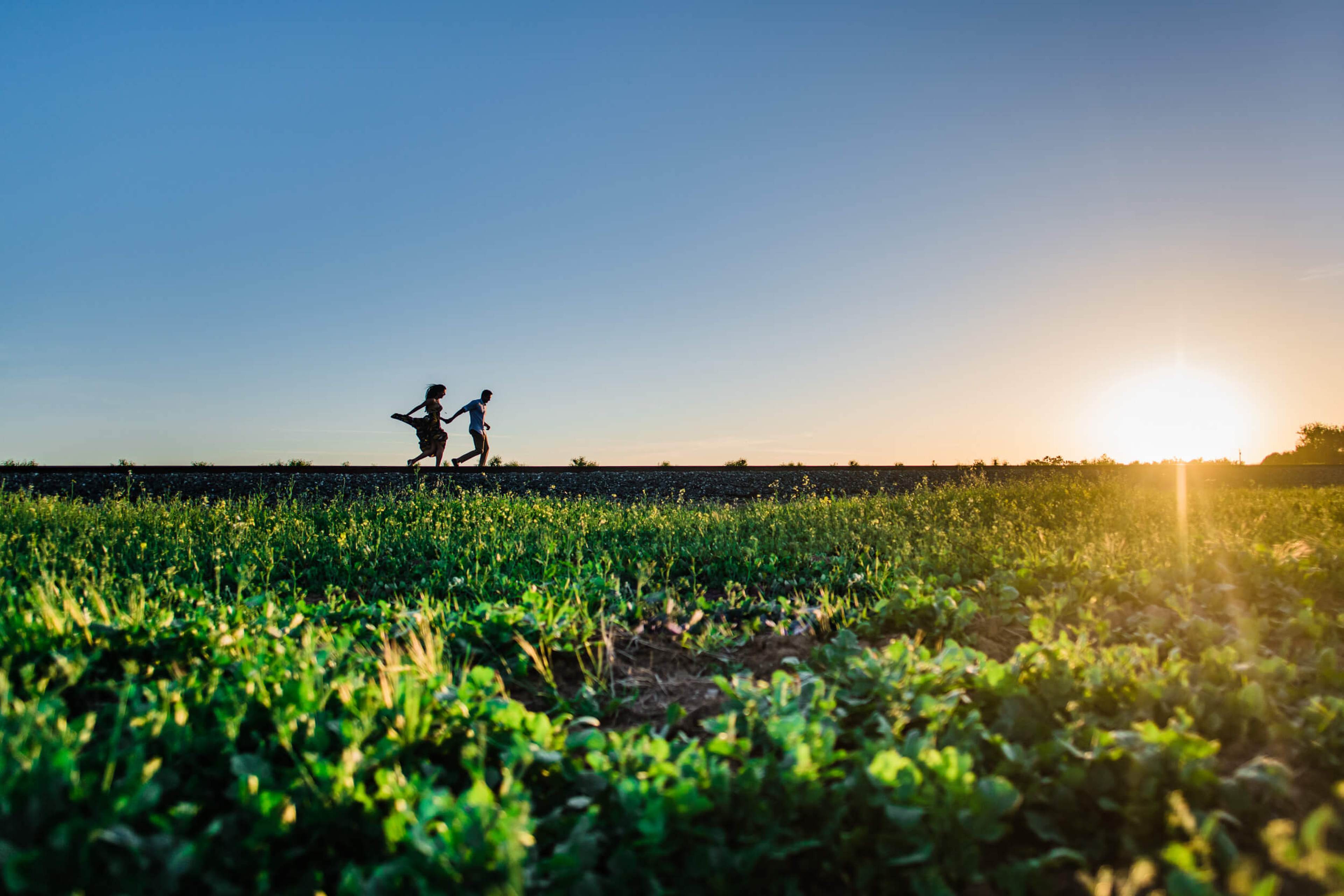 Anu and Raghu run through a sunlit green field at golden hour in California
