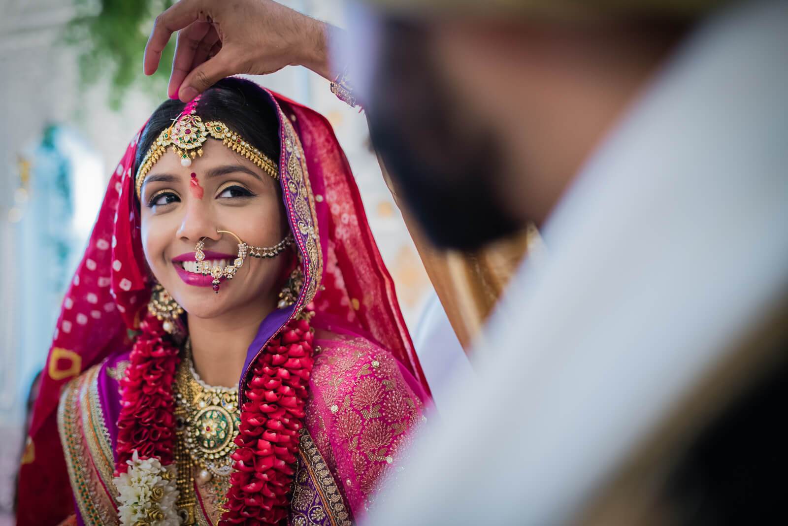 Barkha smiles brightly in traditional red bridal attire with gold jewelry and floral garland