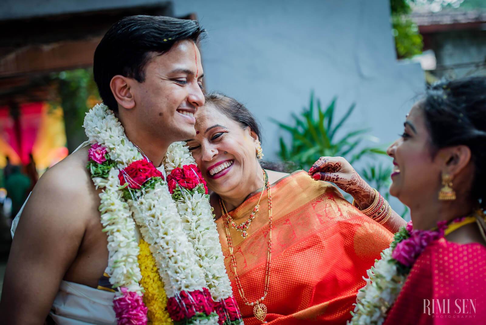 Pooja and Aniket embrace wearing flower garlands at their Bangalore wedding ceremony with family members nearby